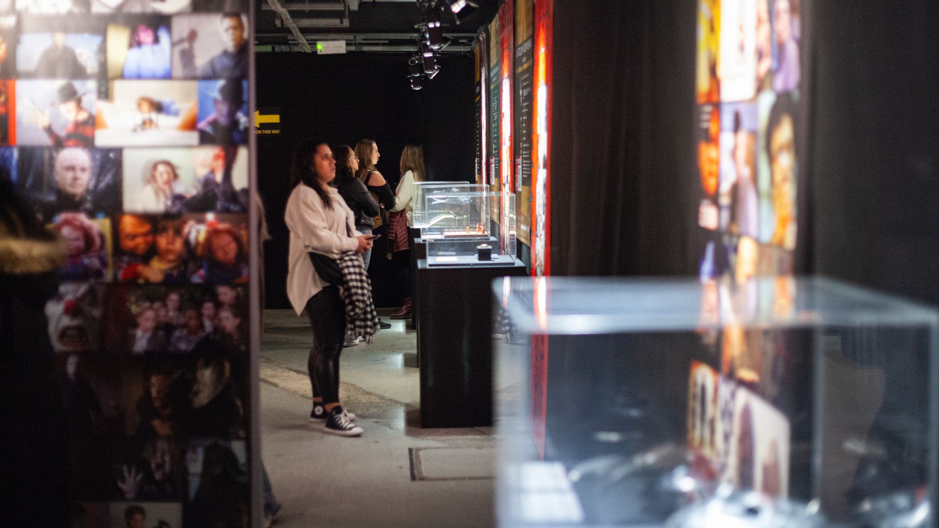 People viewing exhibits in a dimly lit museum or gallery with colorful posters and display cases along the walls.