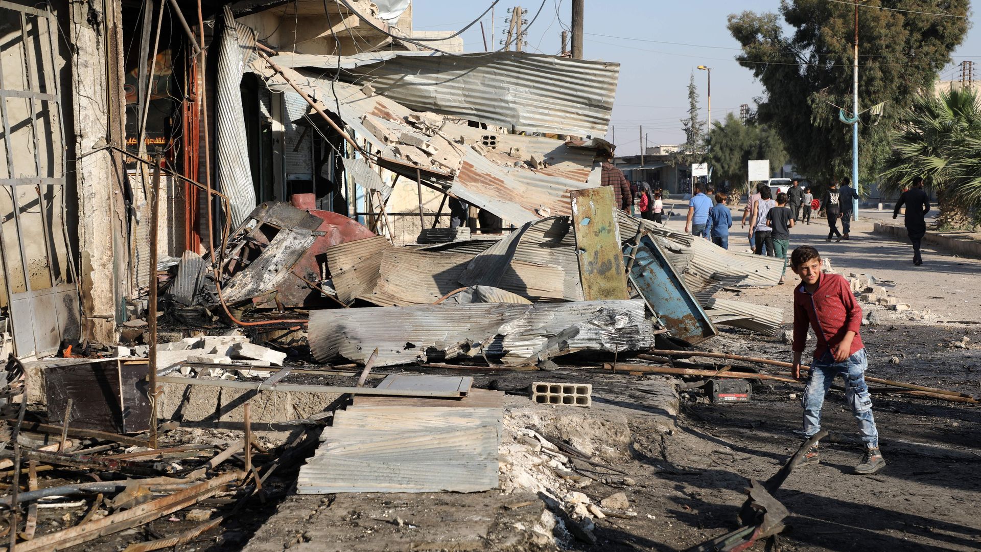 A boy man walks in front of a shop damaged in a car bomb in Syria