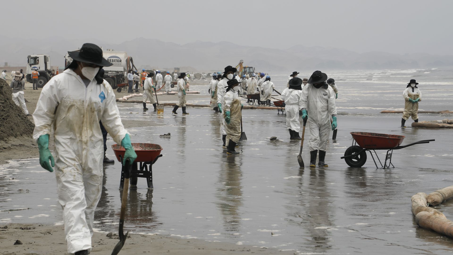 People dressed in protective suits and wearing masks clean up a beach in Peru