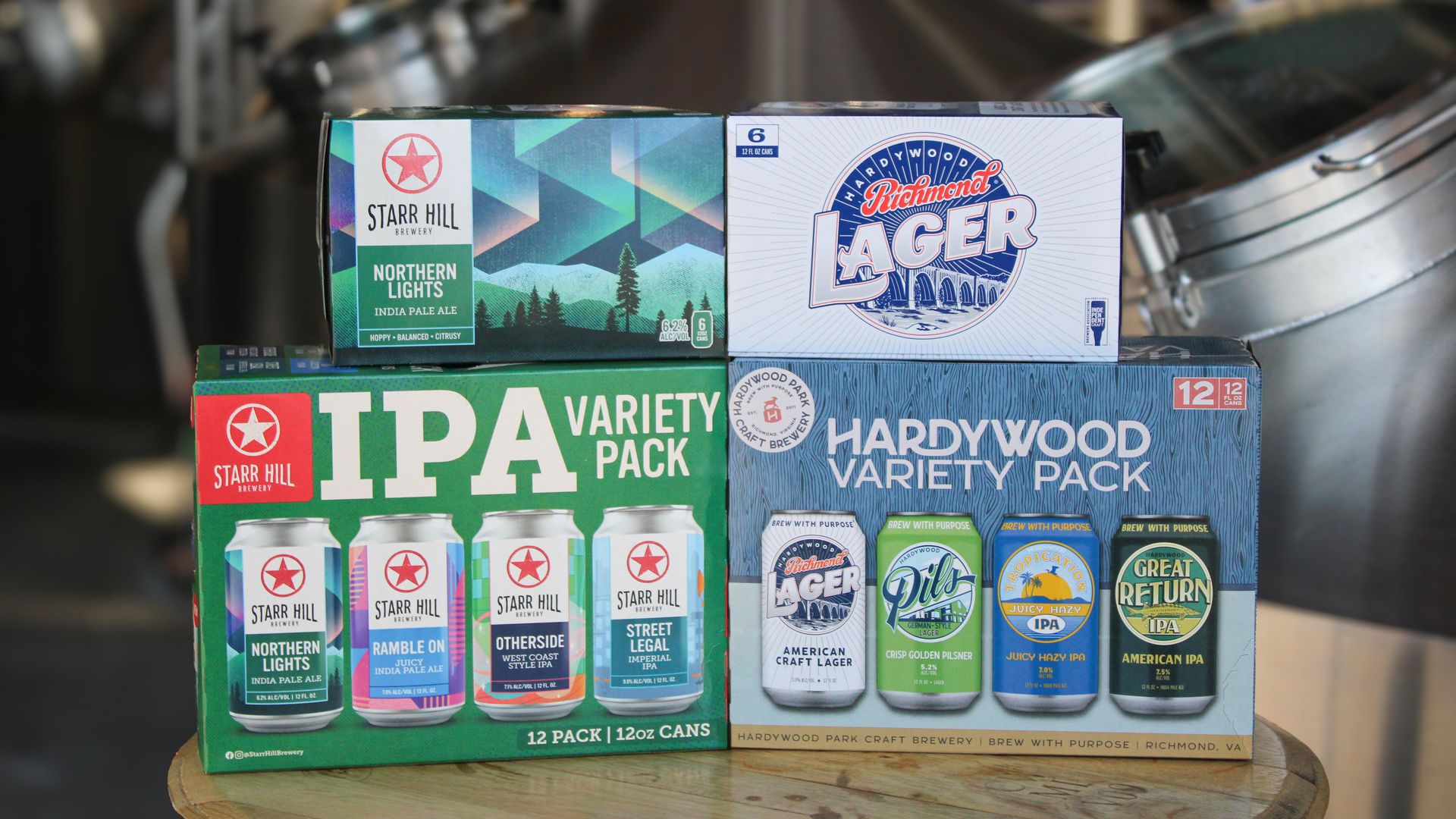 Stack of beer boxes on a wooden table, featuring Starr Hill Northern Lights India Pale Ale and Hardywood Richmond Lager packs; blurred store shelves in the background.