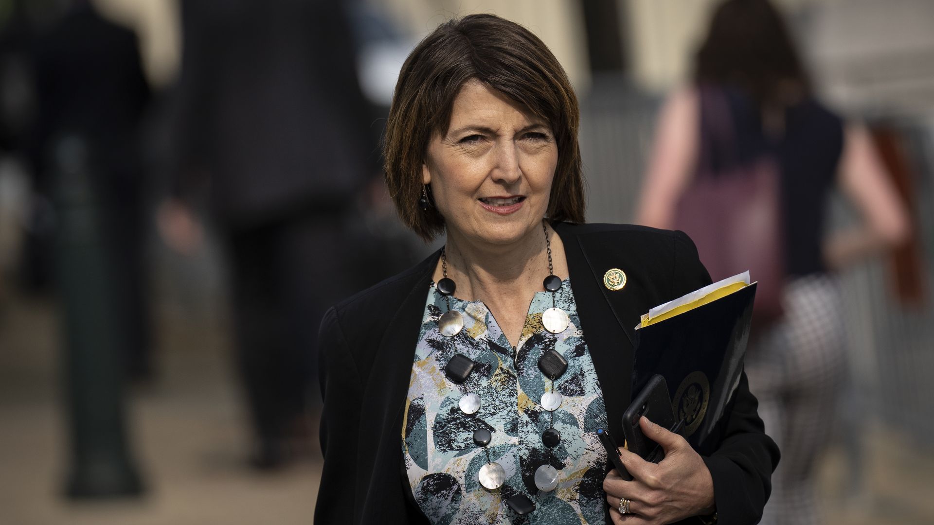 Rep. Cathy McMorris Rodgers, wearing a blue blouse, black blazer and holding a folder.