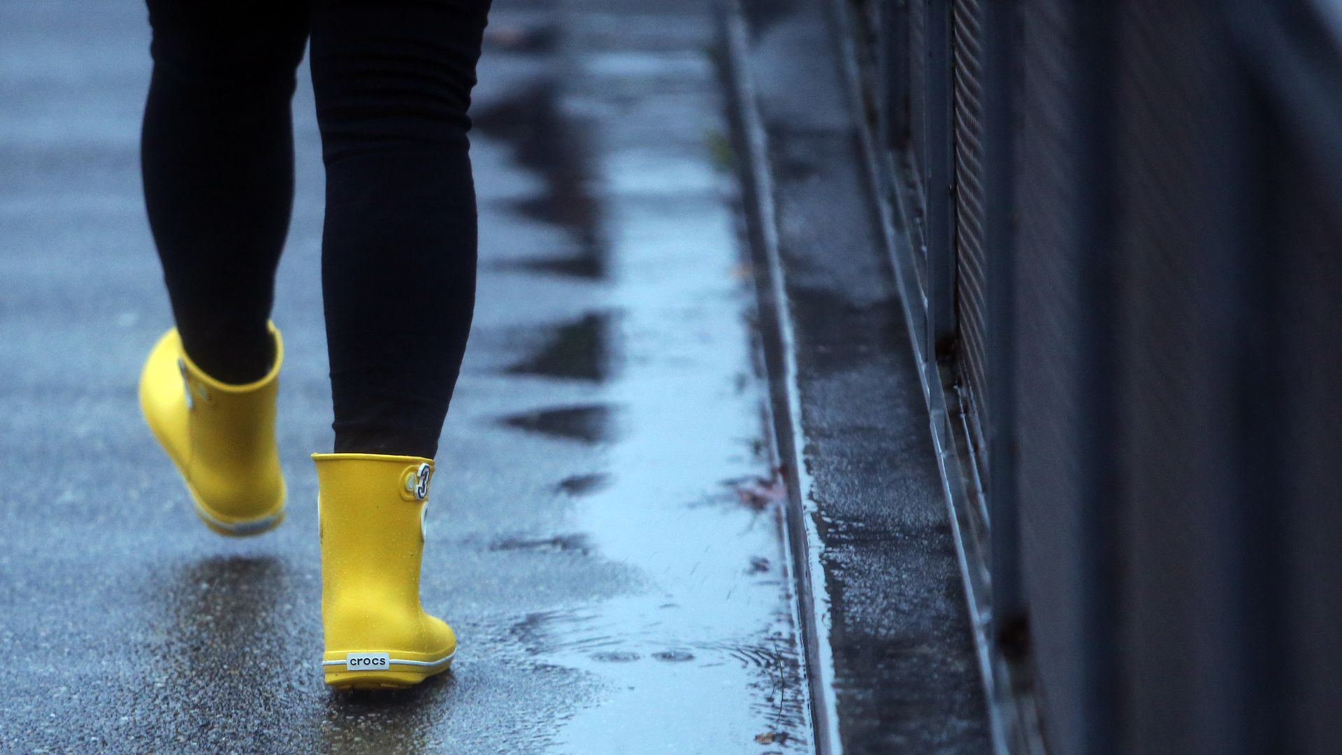 A person with yellow rain boots walks along a rain slicked Seattle sidewalk. 