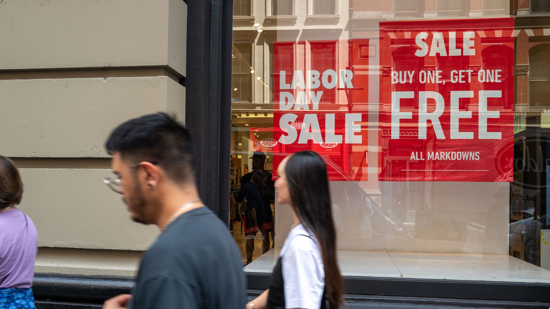 Shoppers walk by a store with signs saying "Labor Day sale" and advertising discounts