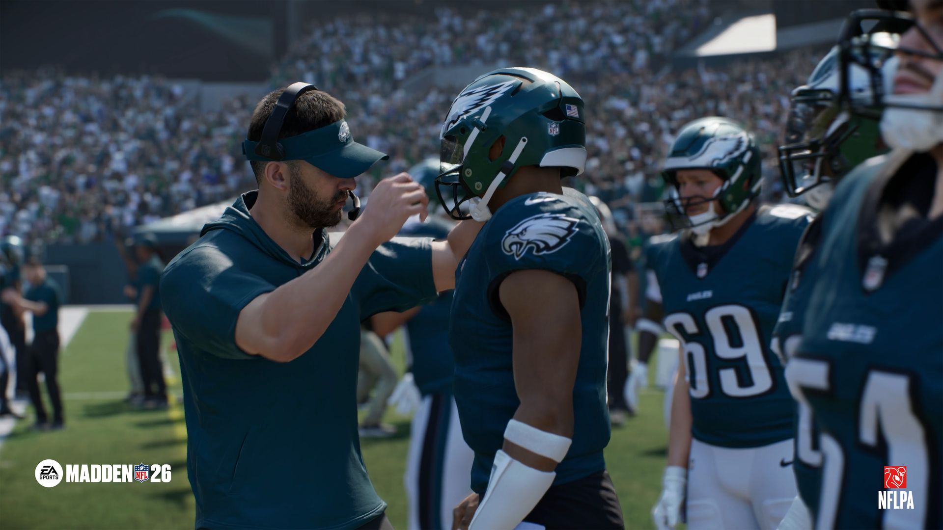 Coach adjusts helmet of Philadelphia Eagles player in dark green uniform on football field with crowd in background, logo for Madden NFL 26 and NFLPA visible.