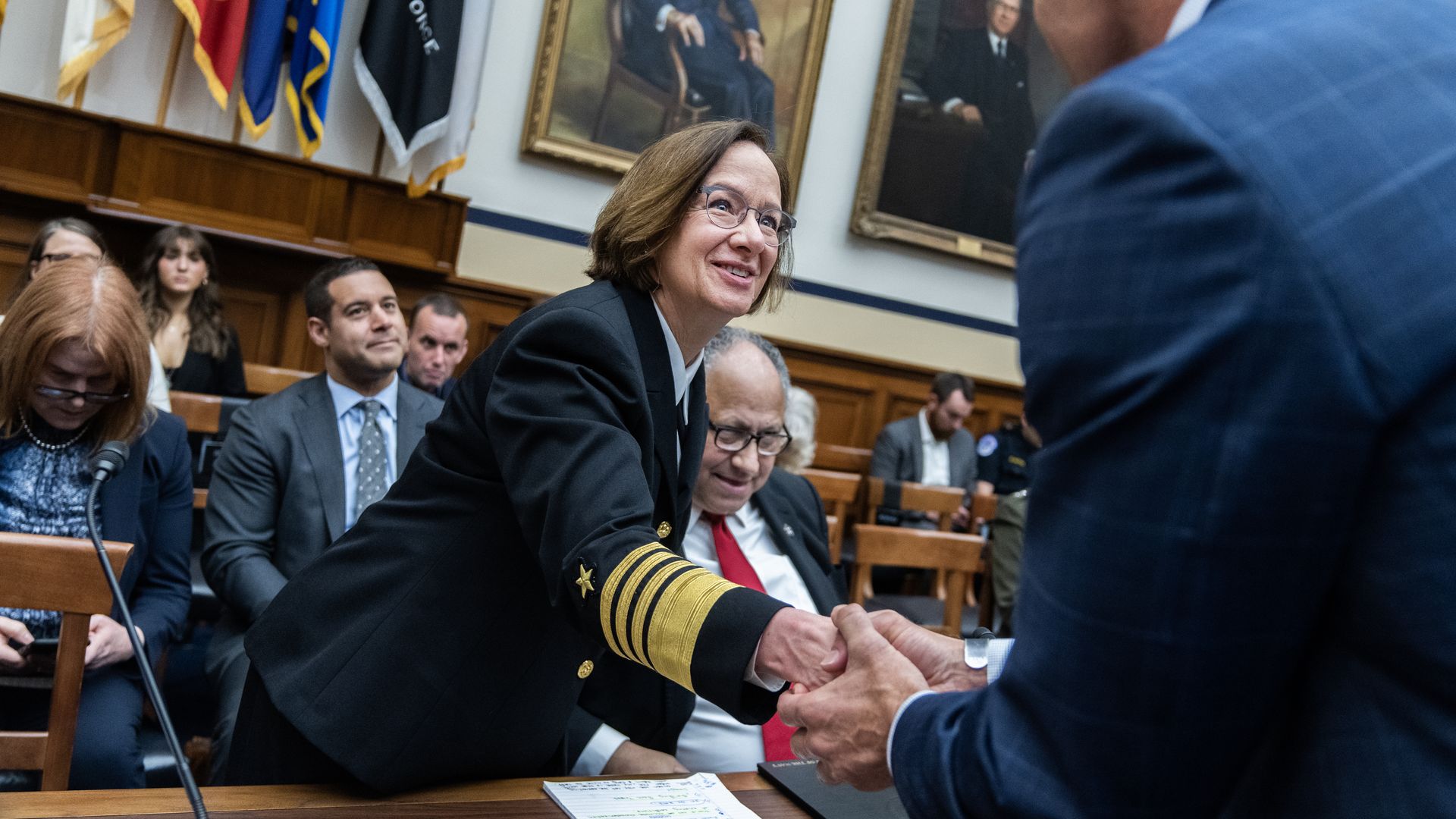 Adm. Lisa Franchetti and Navy Secretary Carlos Del Toro at a congressionally hearing. There are other people in the background and foreground.