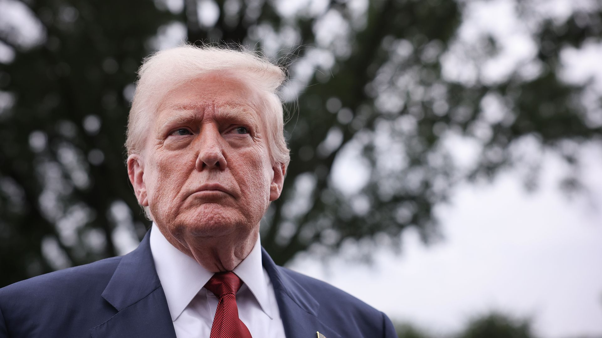 Trump — wearing a white collared shirt, a red tie and a navy suit — looks on as reporters (not pictured) ask questions.