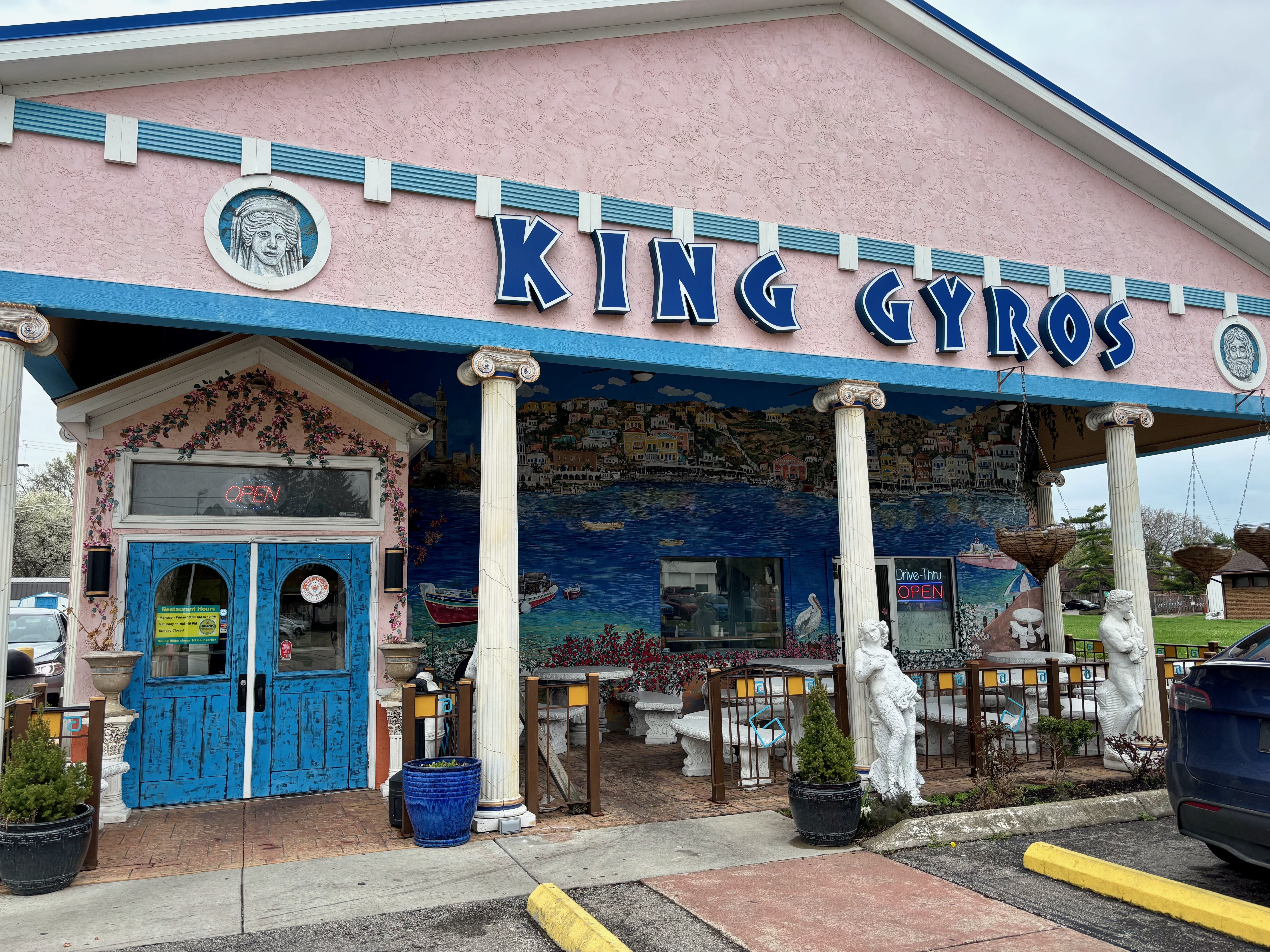 The entrance to King Gyros, a pink building decorated with murals of flowers, scenes of Greece and statues and columns