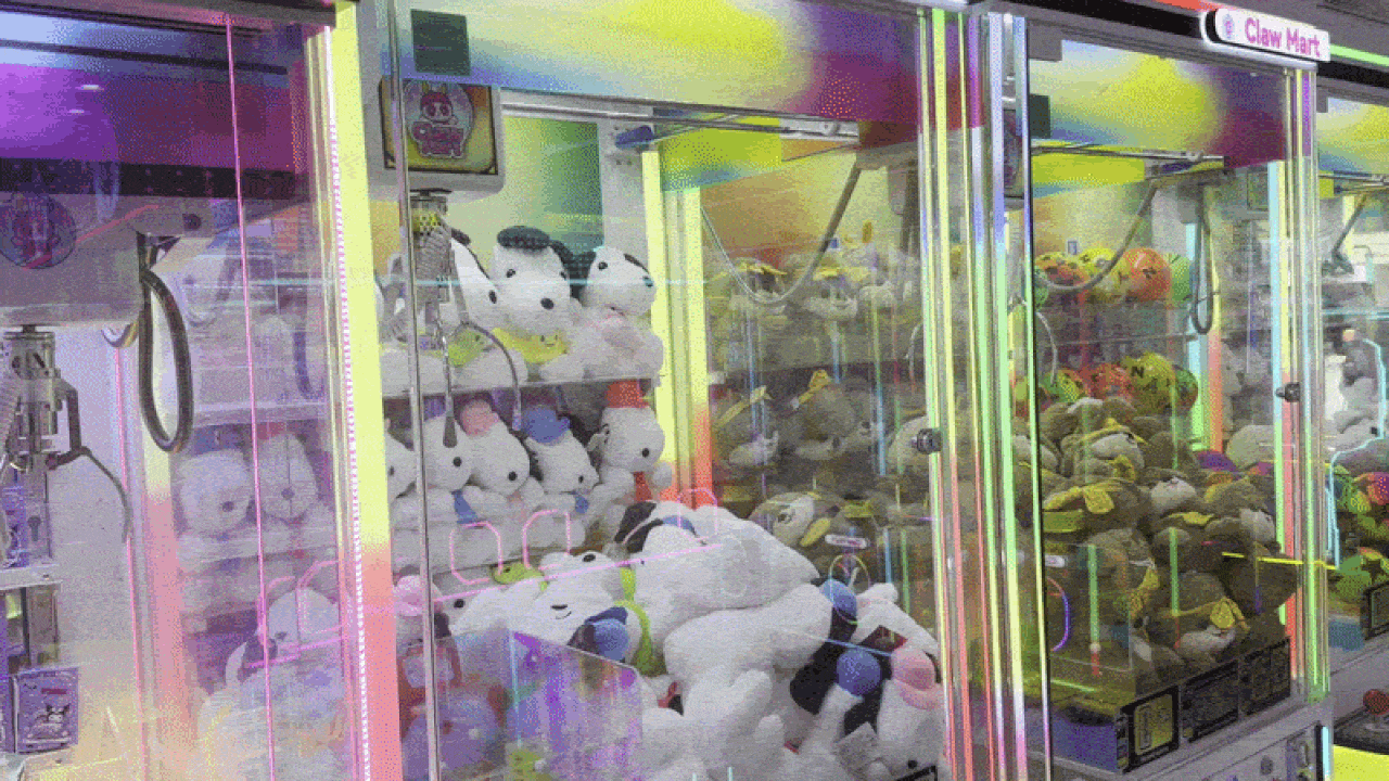 Colorful claw machine arcade with glass doors, stuffed animals inside (white bears, pandas, and other plush toys) glowing under neon lights.