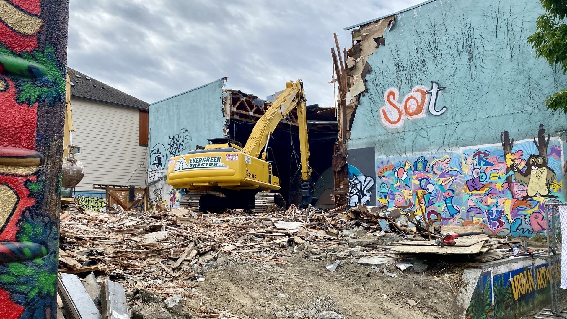 An excavator tears into a blue-teal covered building.