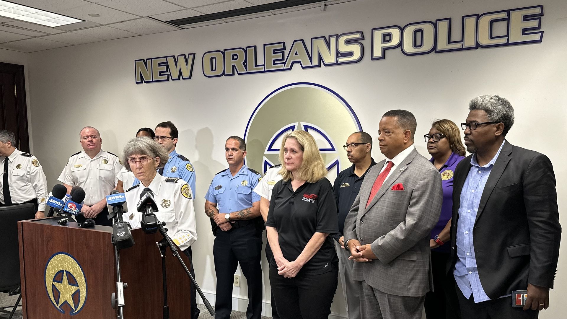 Anne Kirkpatrick speaks at a podium in the NOPD press conference room surrounded by other officials.