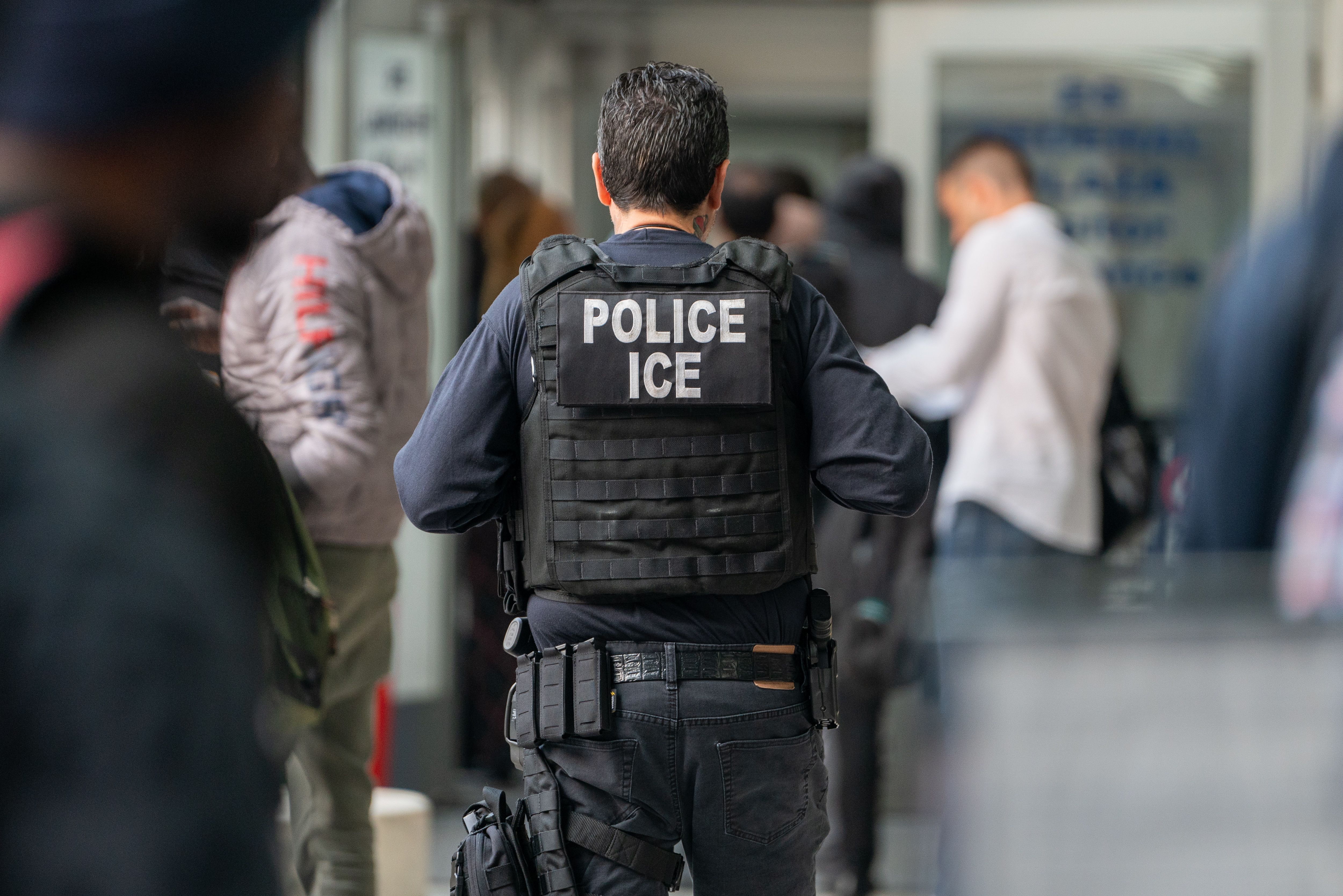 ICE agent watches a large group of asylum seekers waiting to be processed inside the Jacob K. Javits Federal Building in New York City.