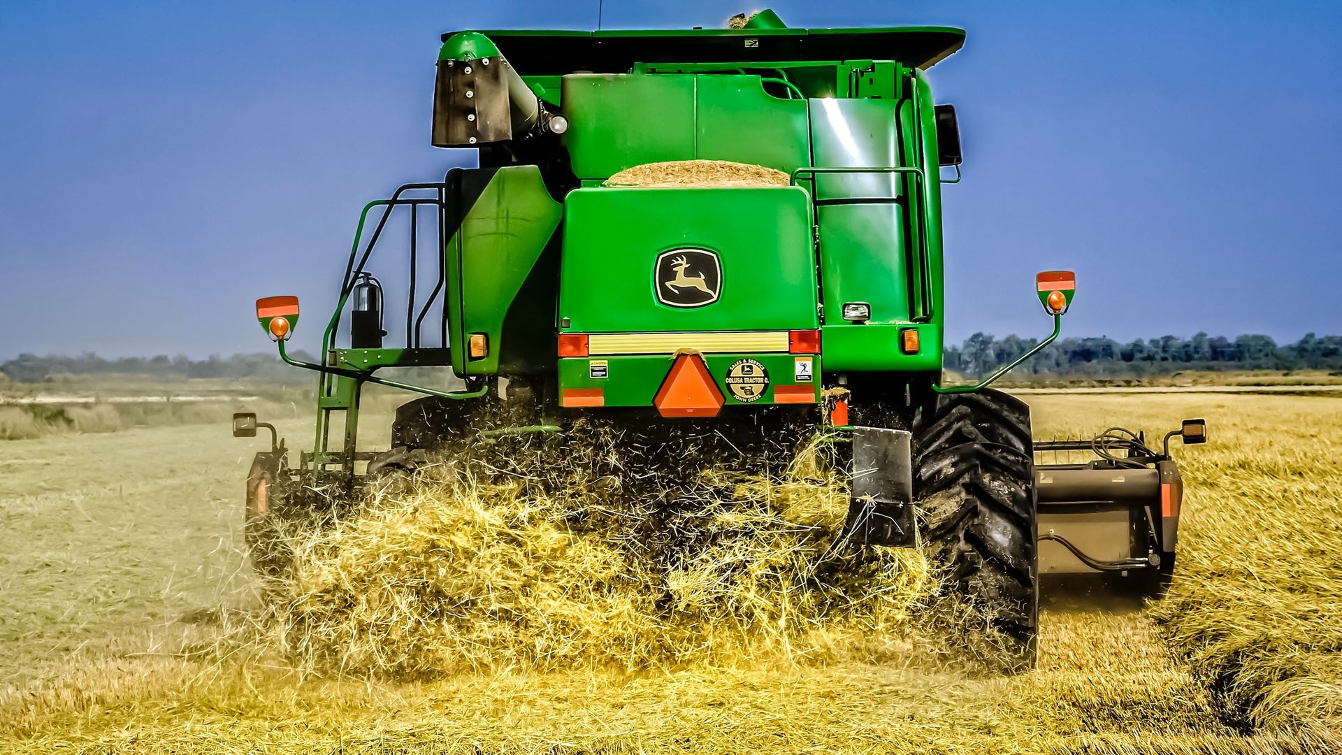 In this image, the back end of a John Deere tractor plows through a field.