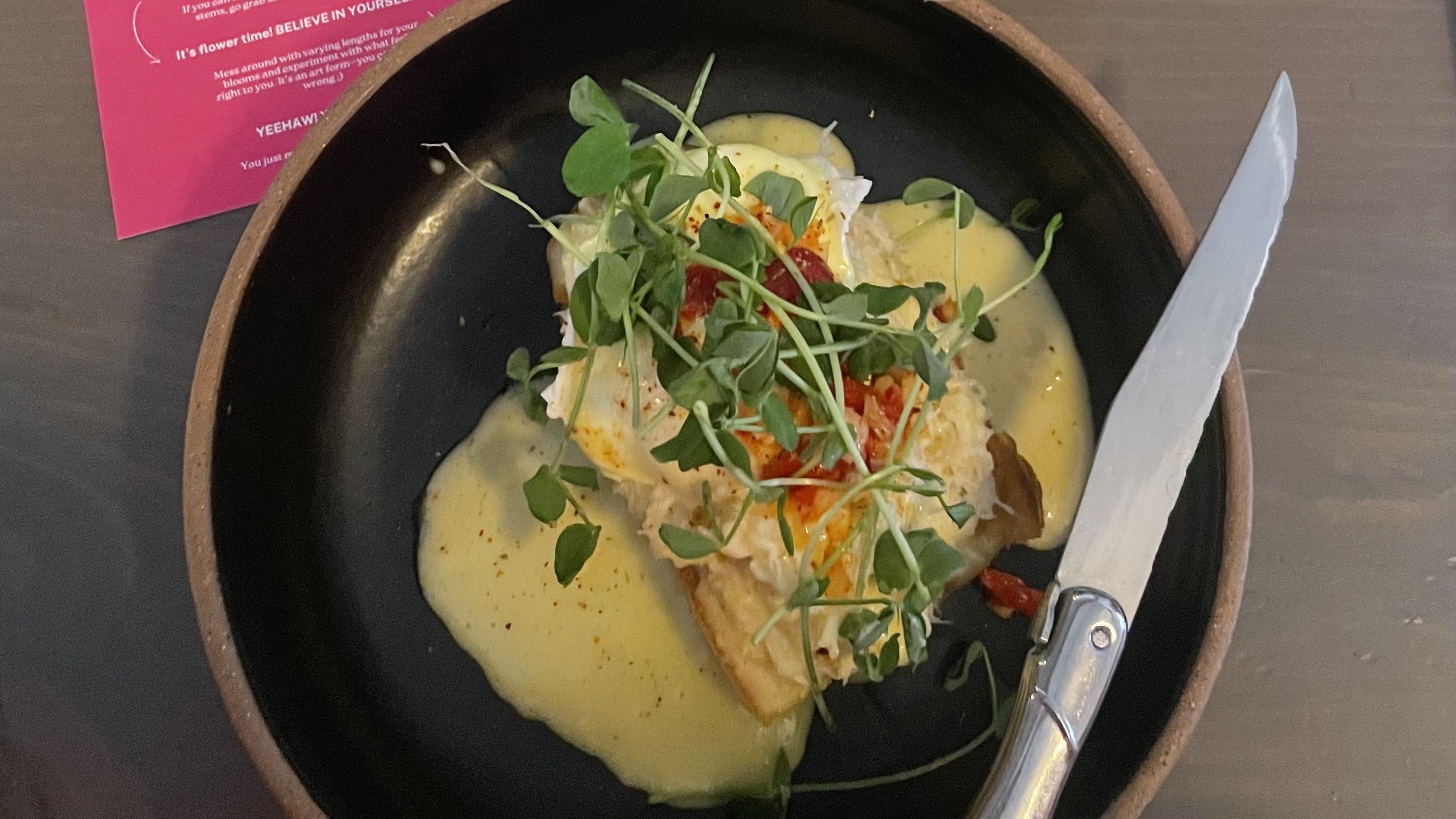 A photo of a black plate with a piece of toast and yellow-hued sauce.