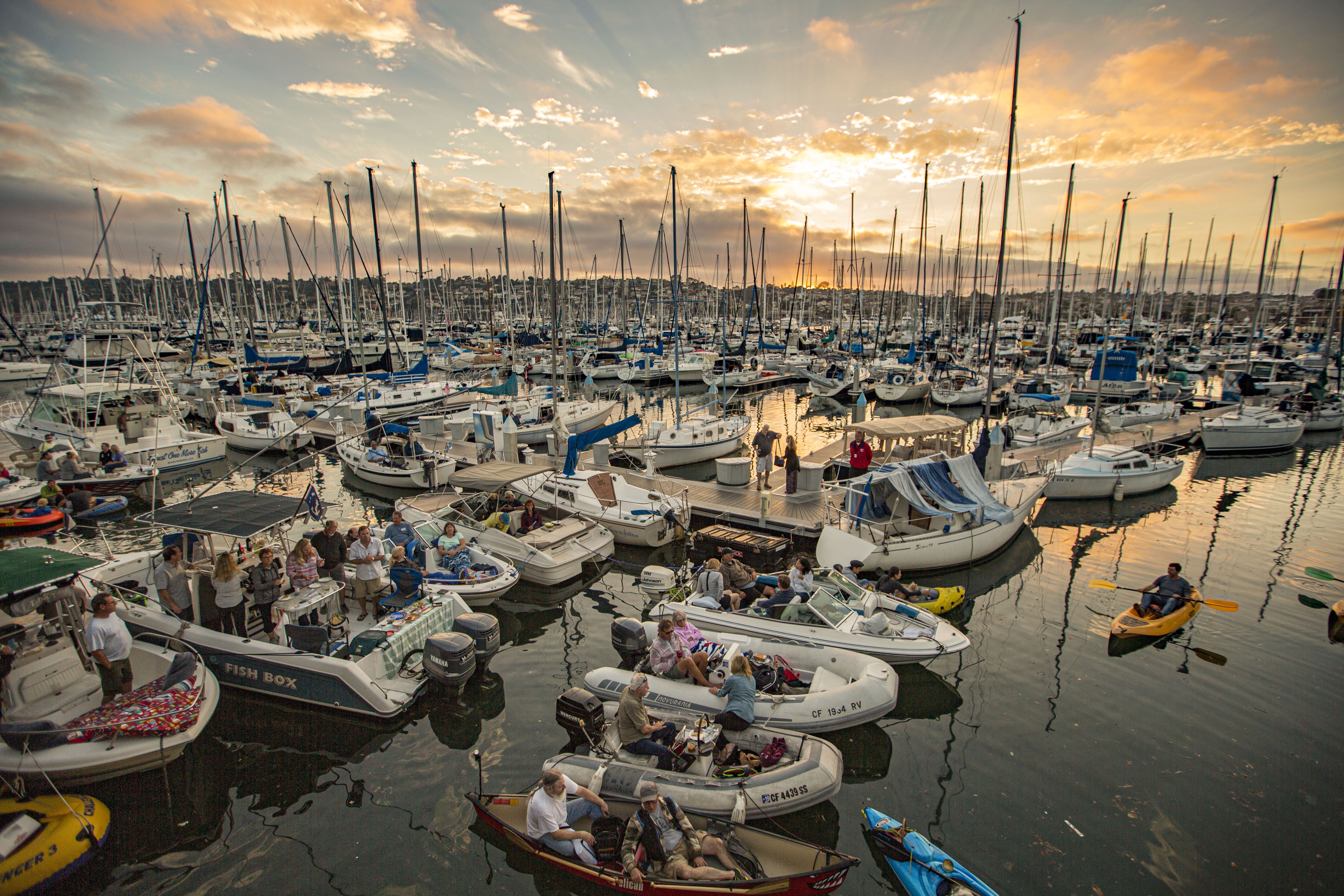 People sit in watercraft on the bay listening to a concert at sunset.