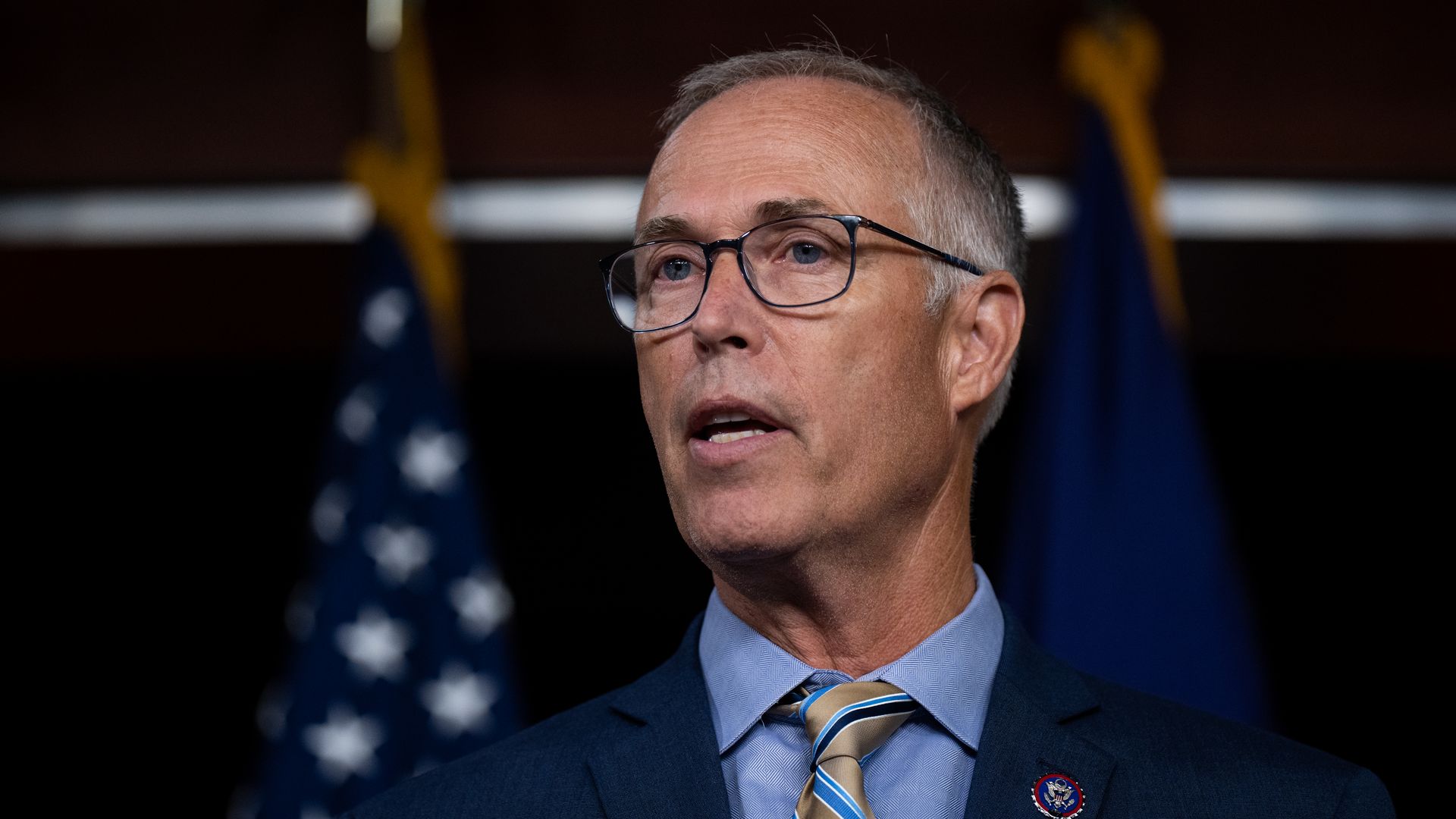 Rep. Jared Huffman, wearing a blue suit and standing in front of American flags.