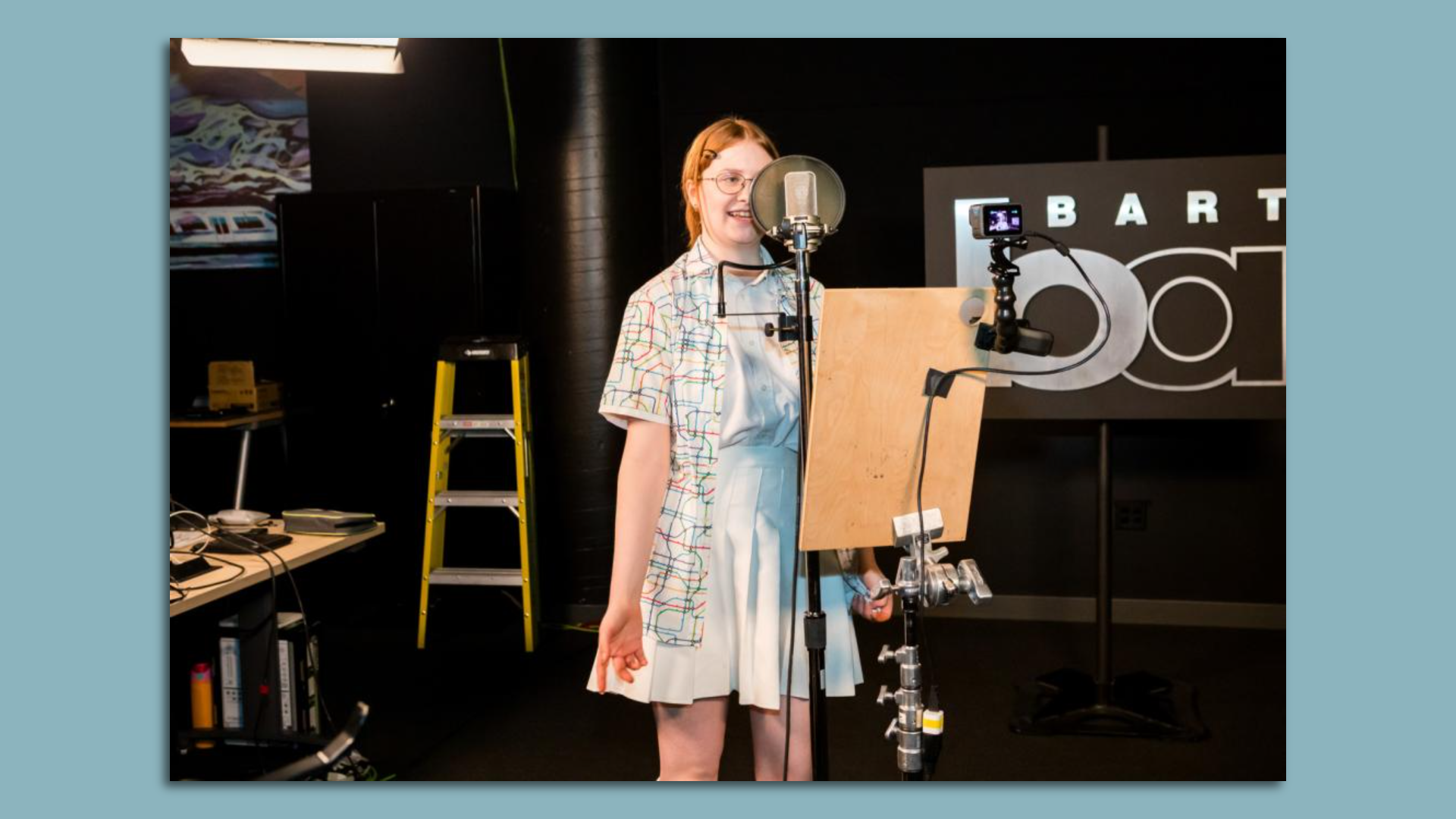 Photo of a young person speaking into a microphone in a recording studio with the BART logo in the back