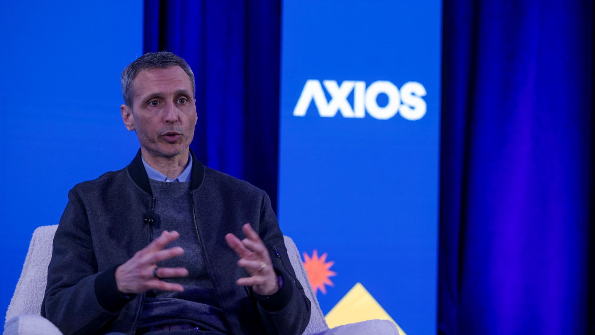 Jimmy Pitaro sits while speaking with his hands in front of him. A backdrop says AXIOS over a blue background. 