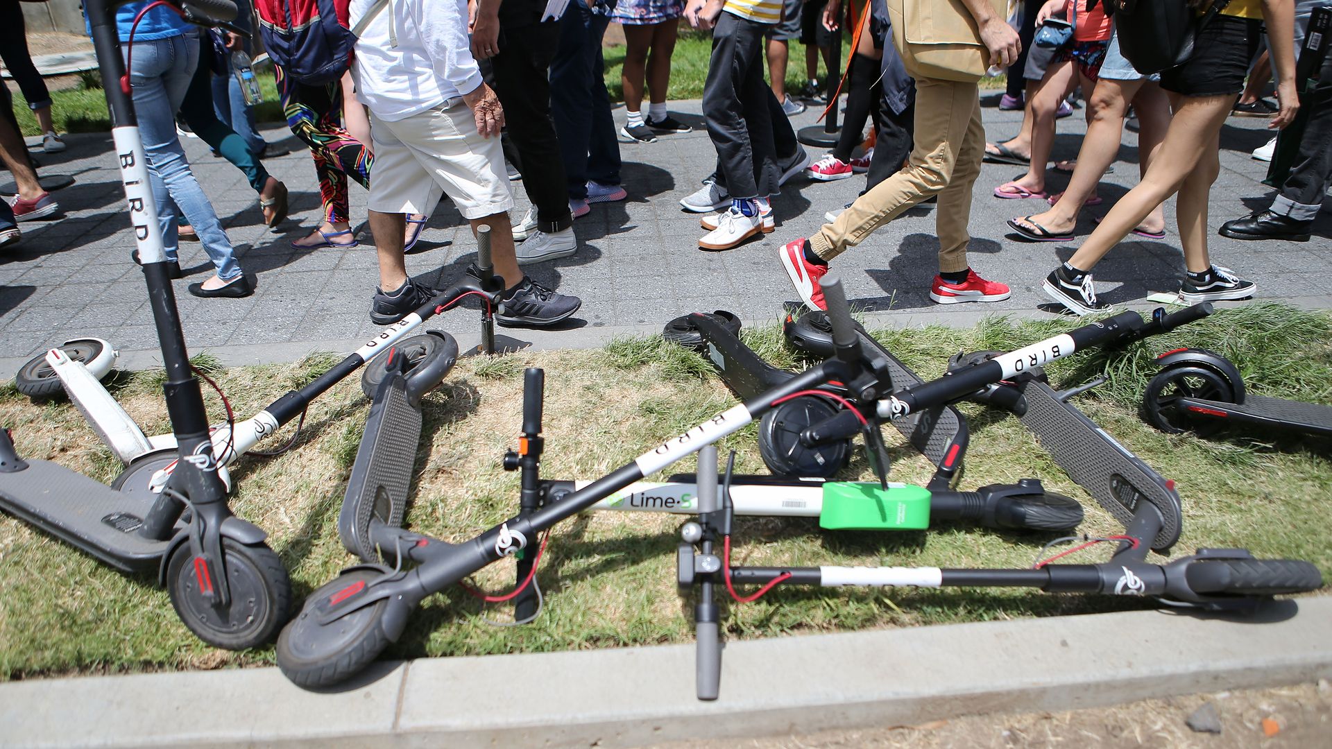 Scooters fallen over on the ground as people walk by
