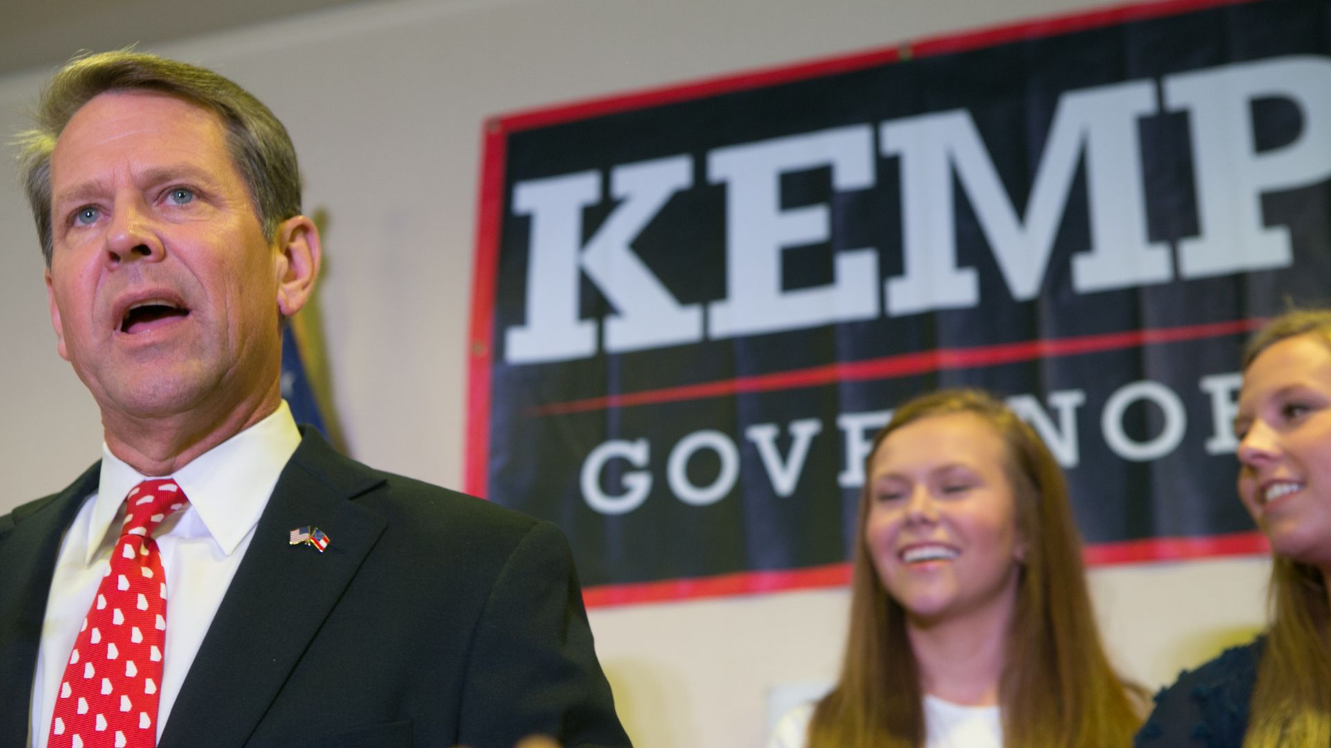 Brian Kemp speaks before a Kemp sign.