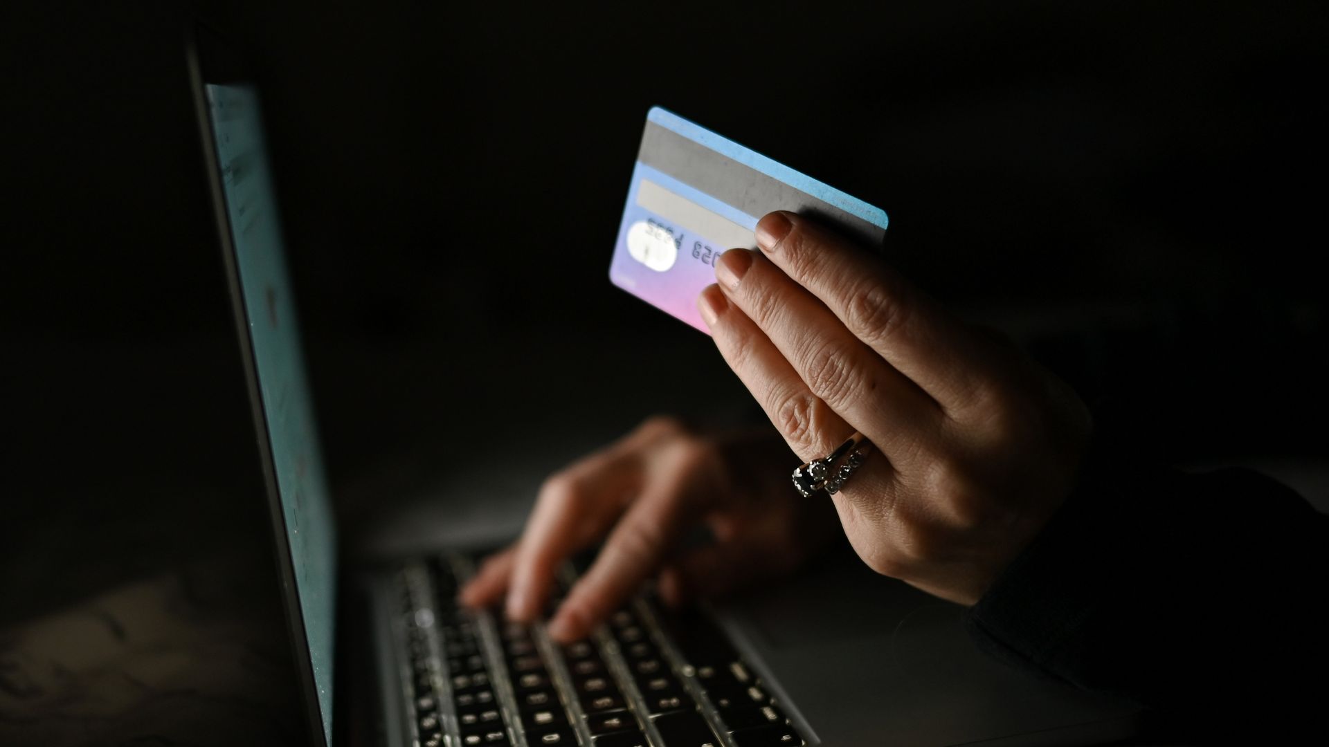 A person holds a credit card with one hand while typing on a laptop with the other hand.