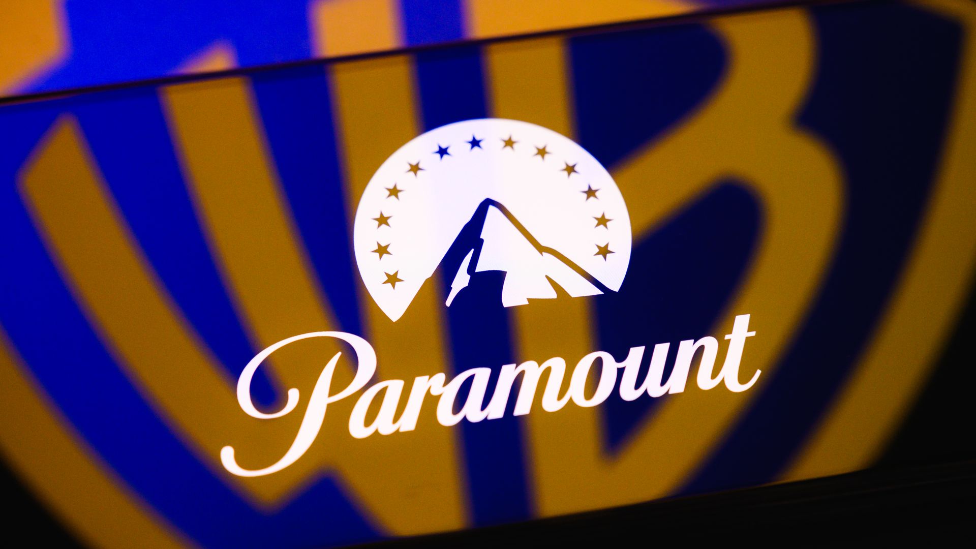 The Paramount logo is displayed on a smartphone screen placed on a reflective surface onto which the Warner Bros. logo is projected.