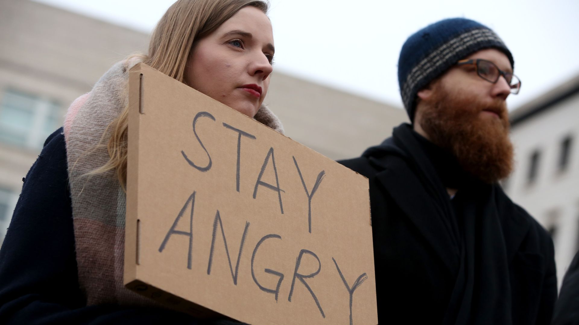 A young woman holds a sign that reads, "Stay Angry." 