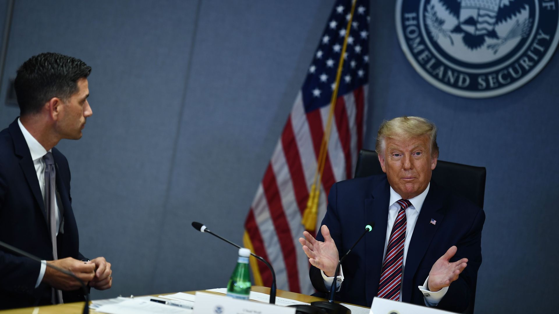 President Trump sits behind a table with the Homeland Security crest behind him 