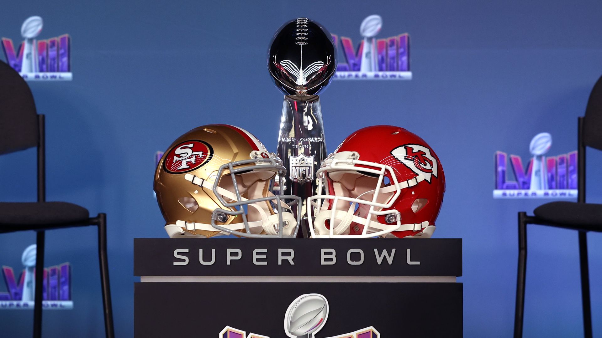 A San Francisco 49ers helmet next to a Kansas City Chiefs helmet with the silver football-shaped Lombardi trophy behind them.