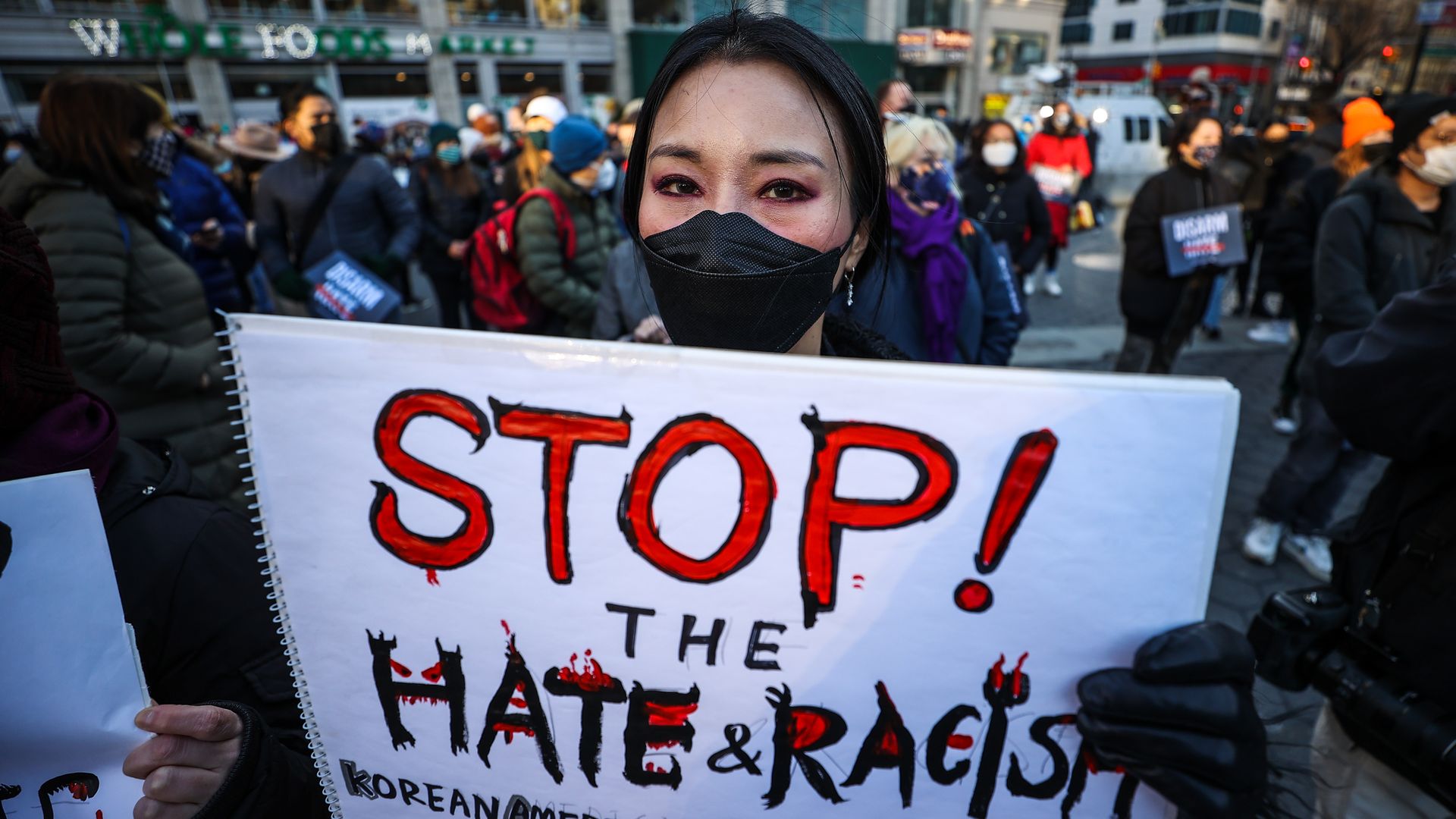 Picture of a woman holding a sign that says, "STOP the HATE & RACISM"