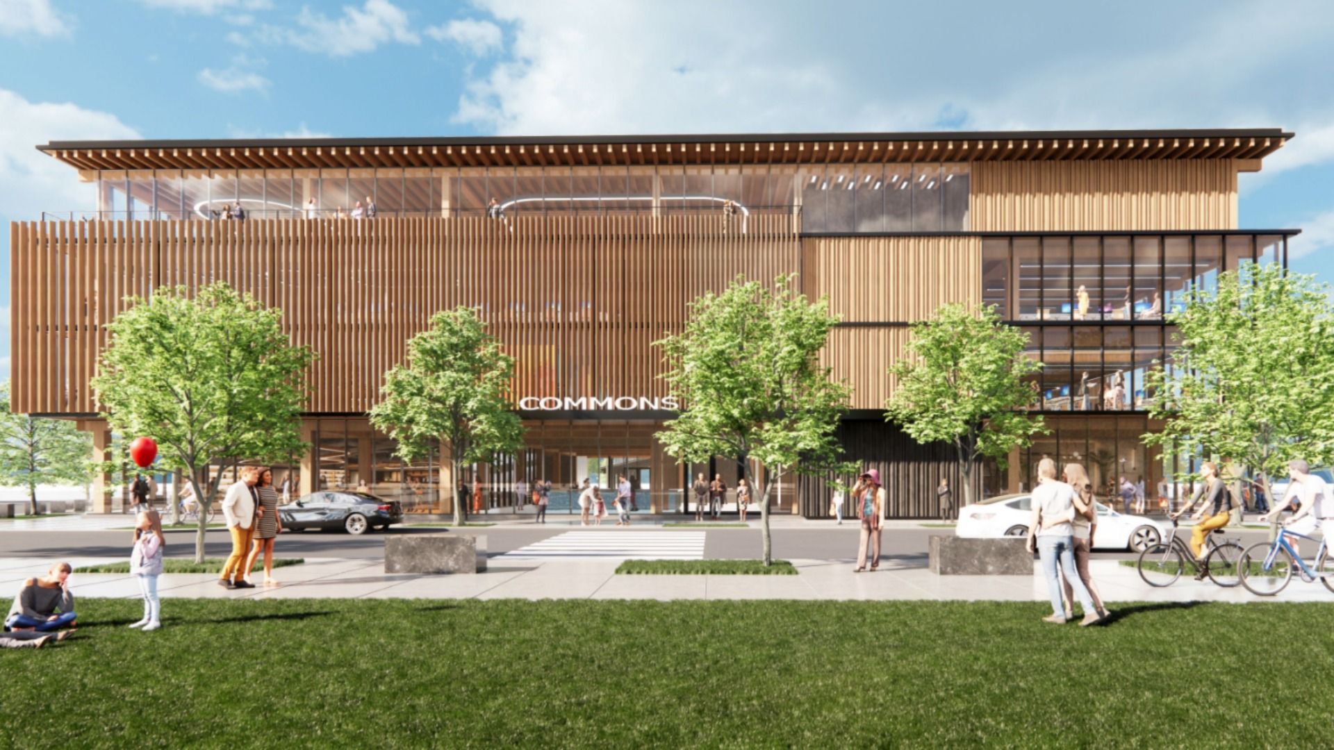 A rendering of a modern three-story wooden building labeled "Commons" with large windows, trees in front, people walking, standing, biking, and a child holding a red balloon on a sunny day.