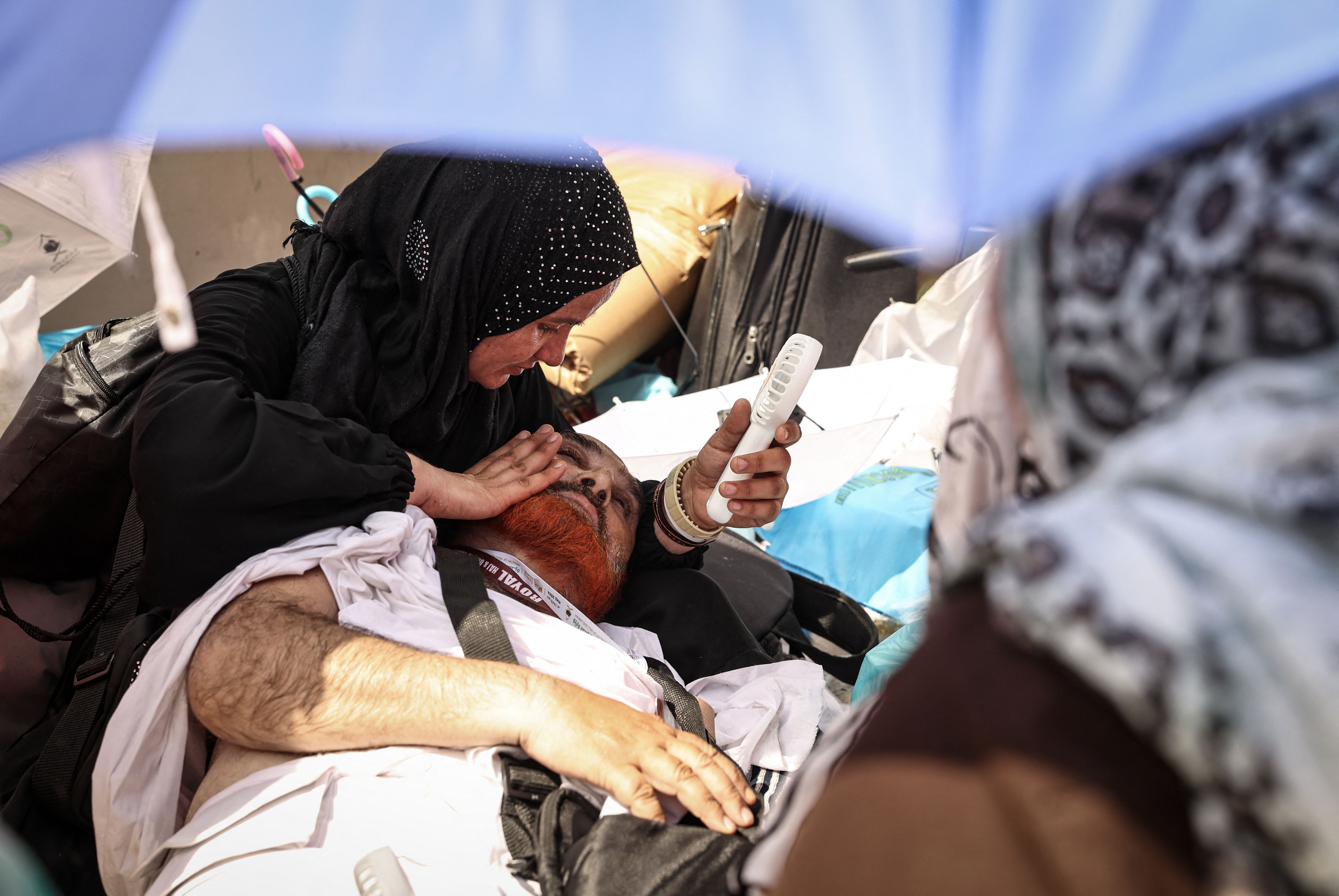 A woman holding a portable fan up to a man's face who is laying on the ground. 