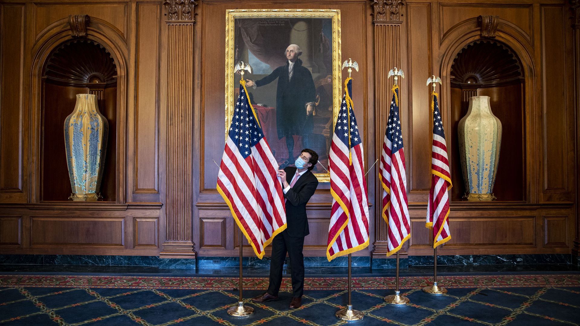 A congressional aide is seen adjusting flags before a swearing-in ceremony.
