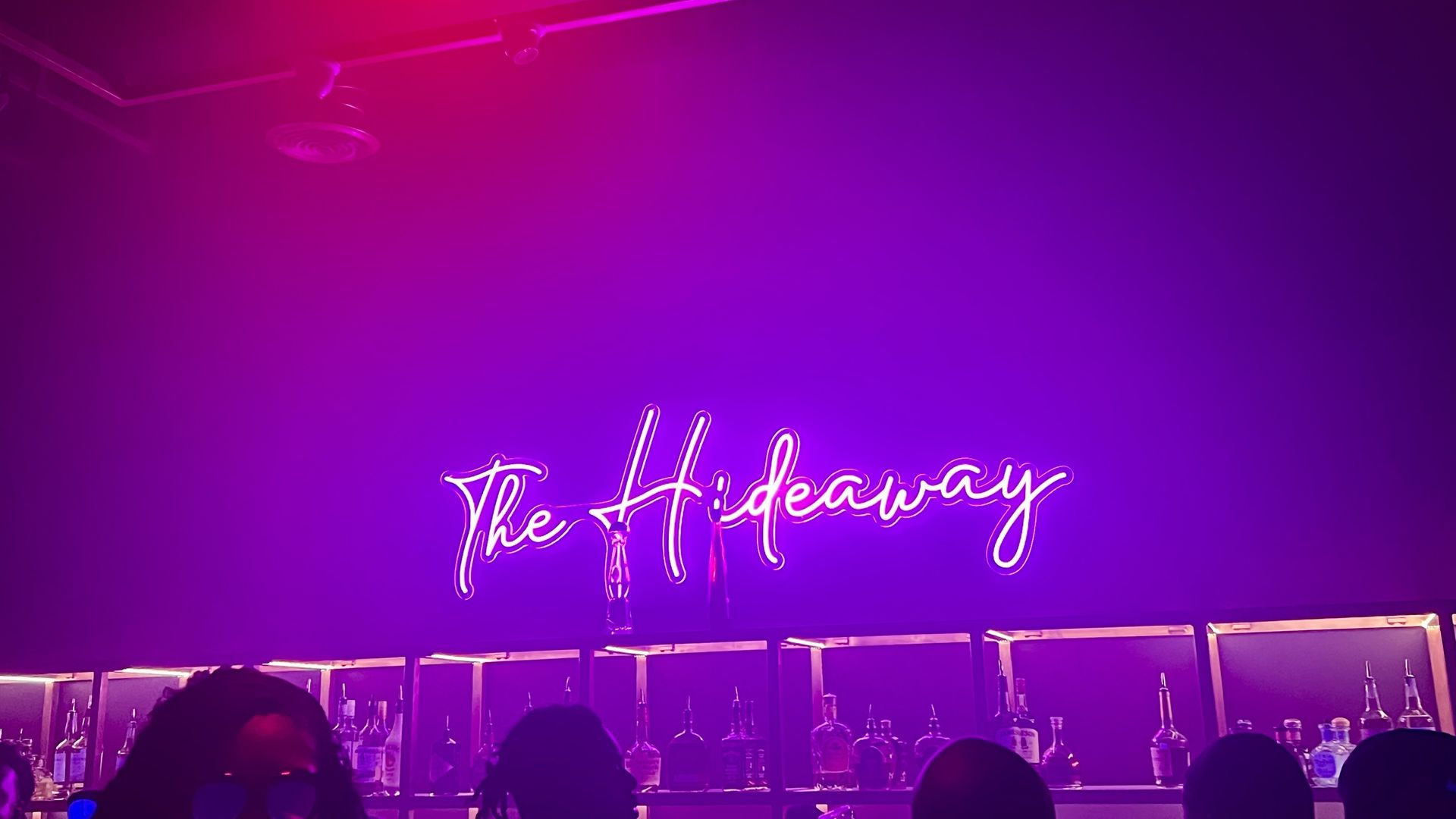 a pinkish purple neon sign that says "The Hideaway" in cursive