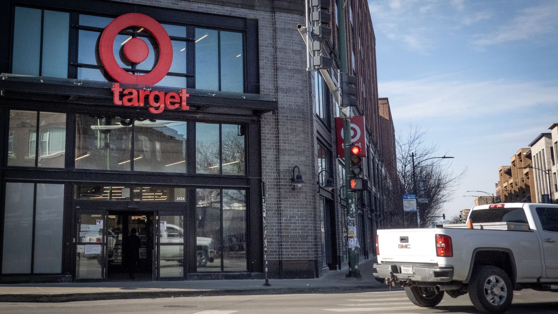Urban street scene with a Target storefront and large red logo; a white GMC pickup is parked on the curb under a clear blue sky.