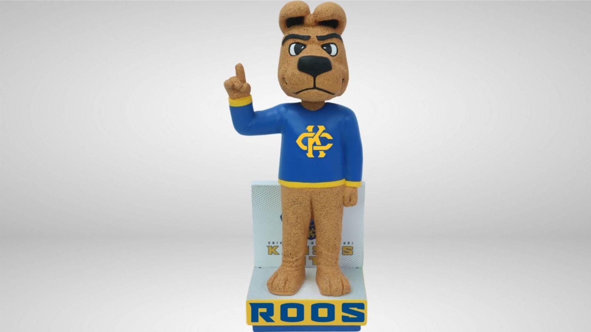Figurine of a brown kangaroo wearing a blue shirt with yellow accents and a logo, standing on a base that reads "ROOS" in blue letters on yellow background.