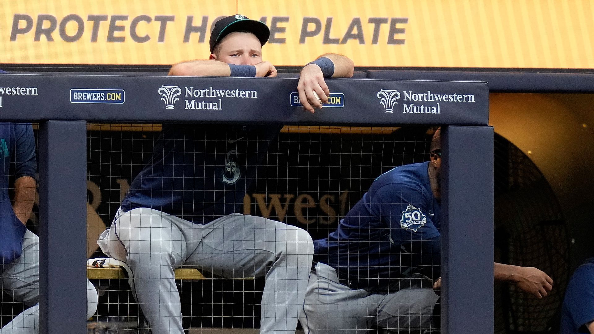 Cal Raleigh sits in the Mariners dugout, staring toward the field with a glum expression after being pulled from the game.
