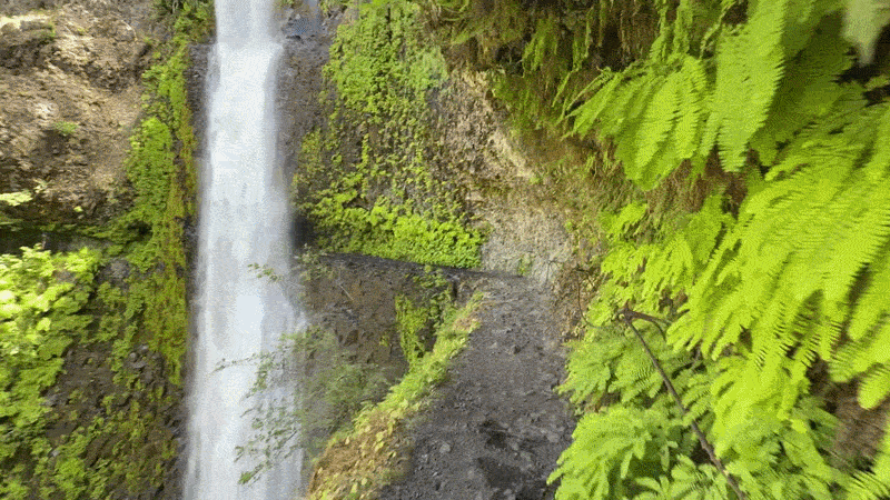 Animated gif shows point of view video of going through a tunnel carved in a cliff behind a waterfall.