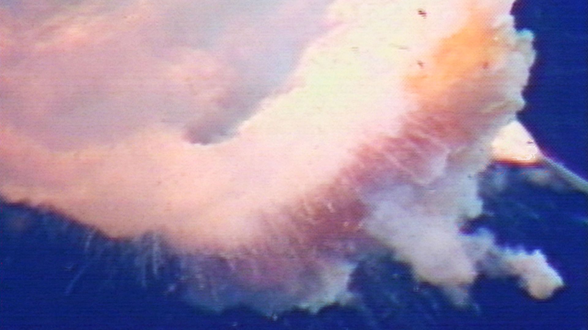 A space shuttle explodes in a blue sky. 