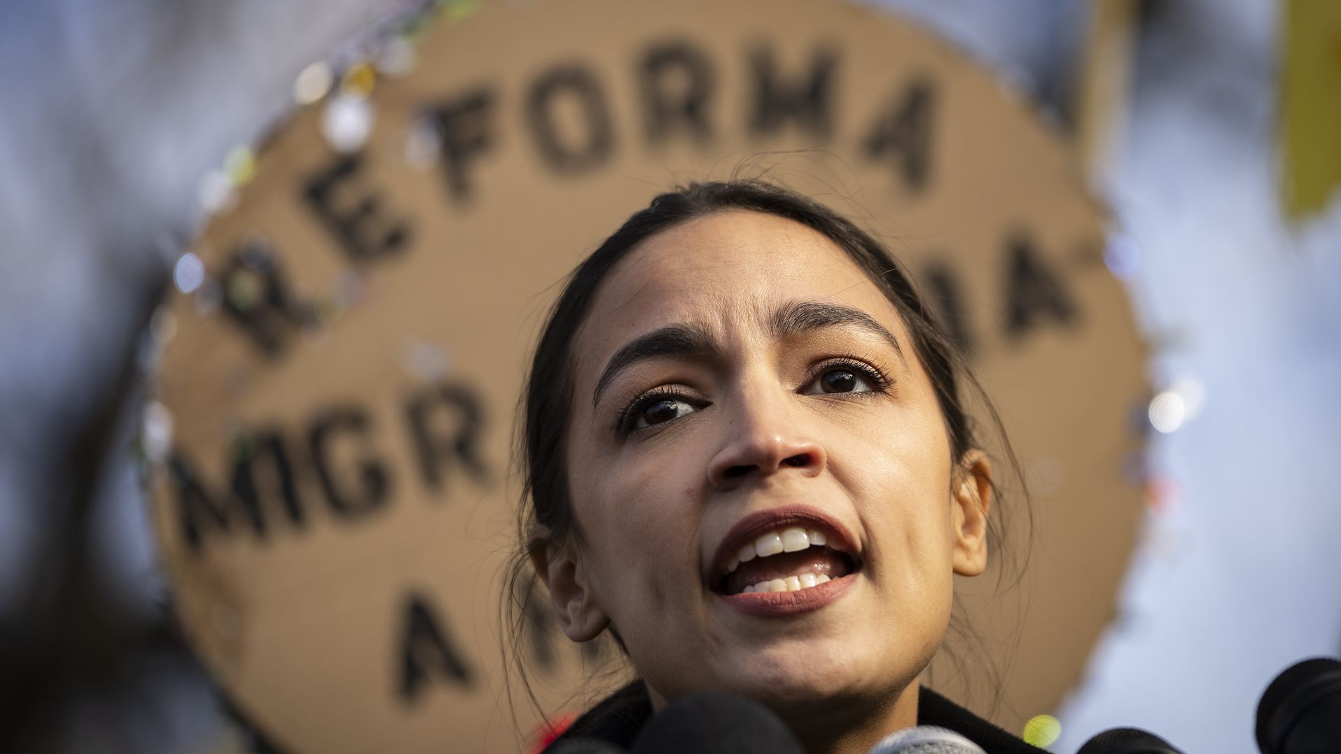 Photo of Alexandria Ocasio-Cortez speaking into a mic at an immigration rally