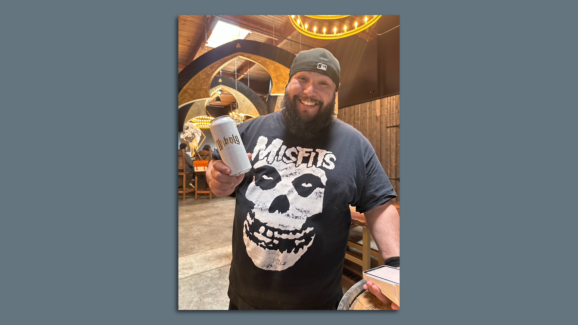 Man in a Misfits shirt and beanie in a bar holding a white can of Unholy Water