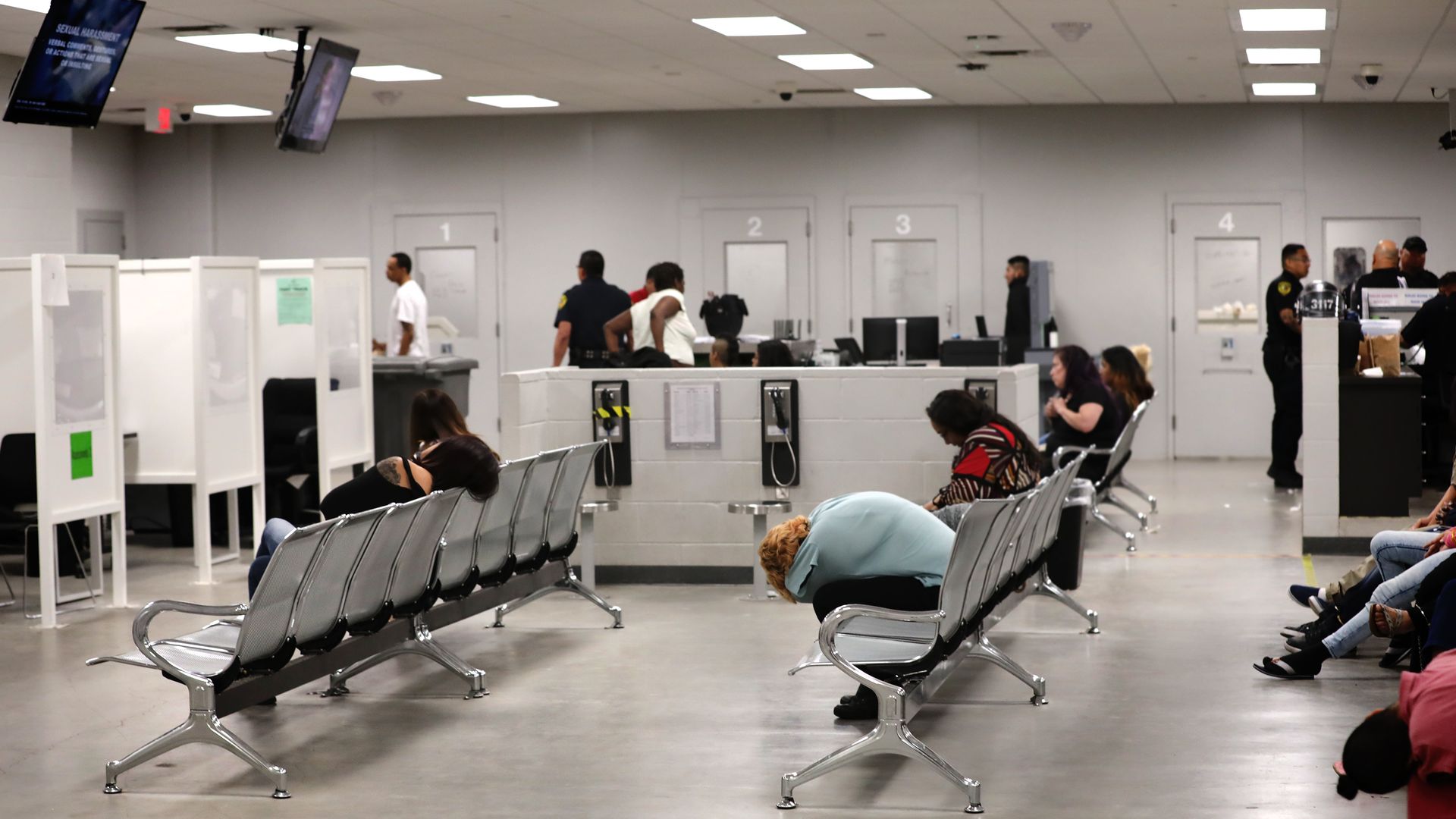The woman's side of intake at the Bexar County Adult Detention Center in 2019. The photo shows a room with gray walls and gray floors, bright overhead lighting, and rows of chairs filled with a few people who look tired.