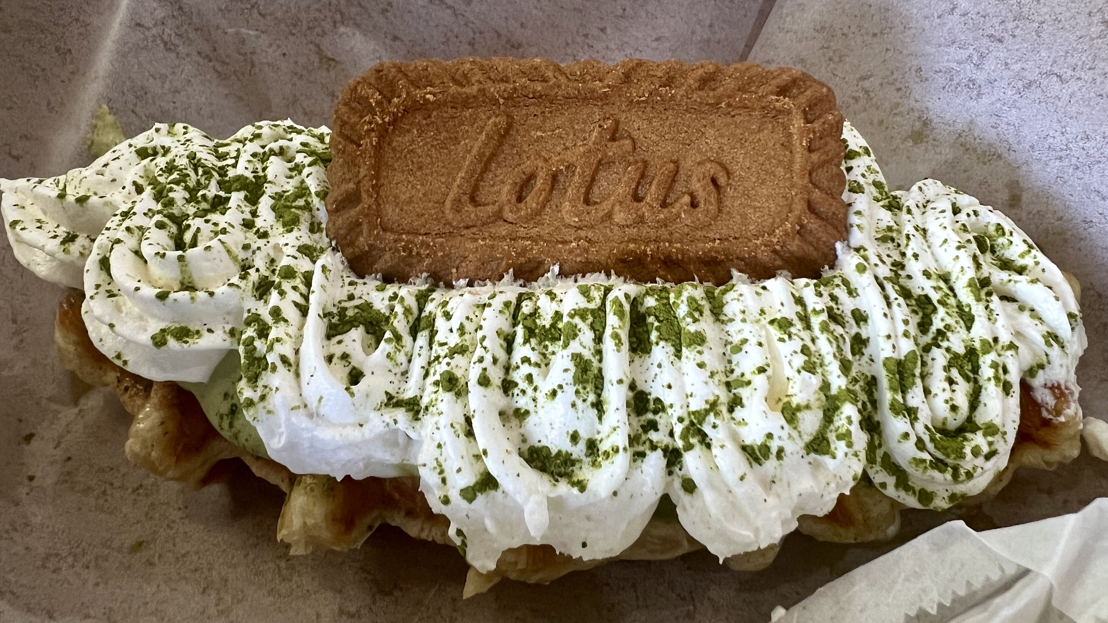 A waffle shaped like a croissant with white cream on it and a green powder spinkled over it