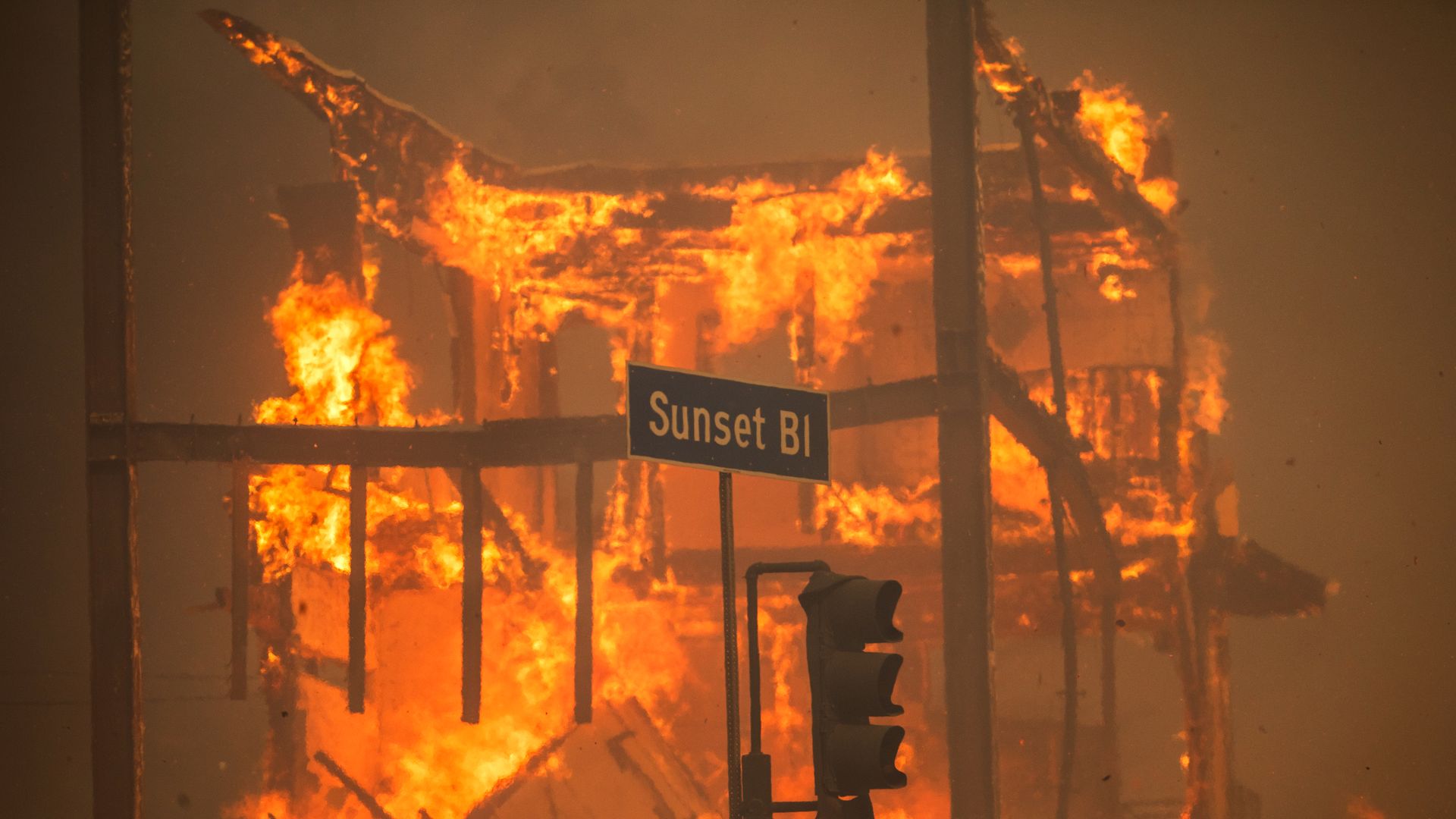 Flames from the Palisades Fire burn a building, with a Sunset Boulevard sign and traffic lights outside amid a powerful windstorm on January 8, 2025 in the Pacific Palisades neighborhood of Los Angeles, California.
