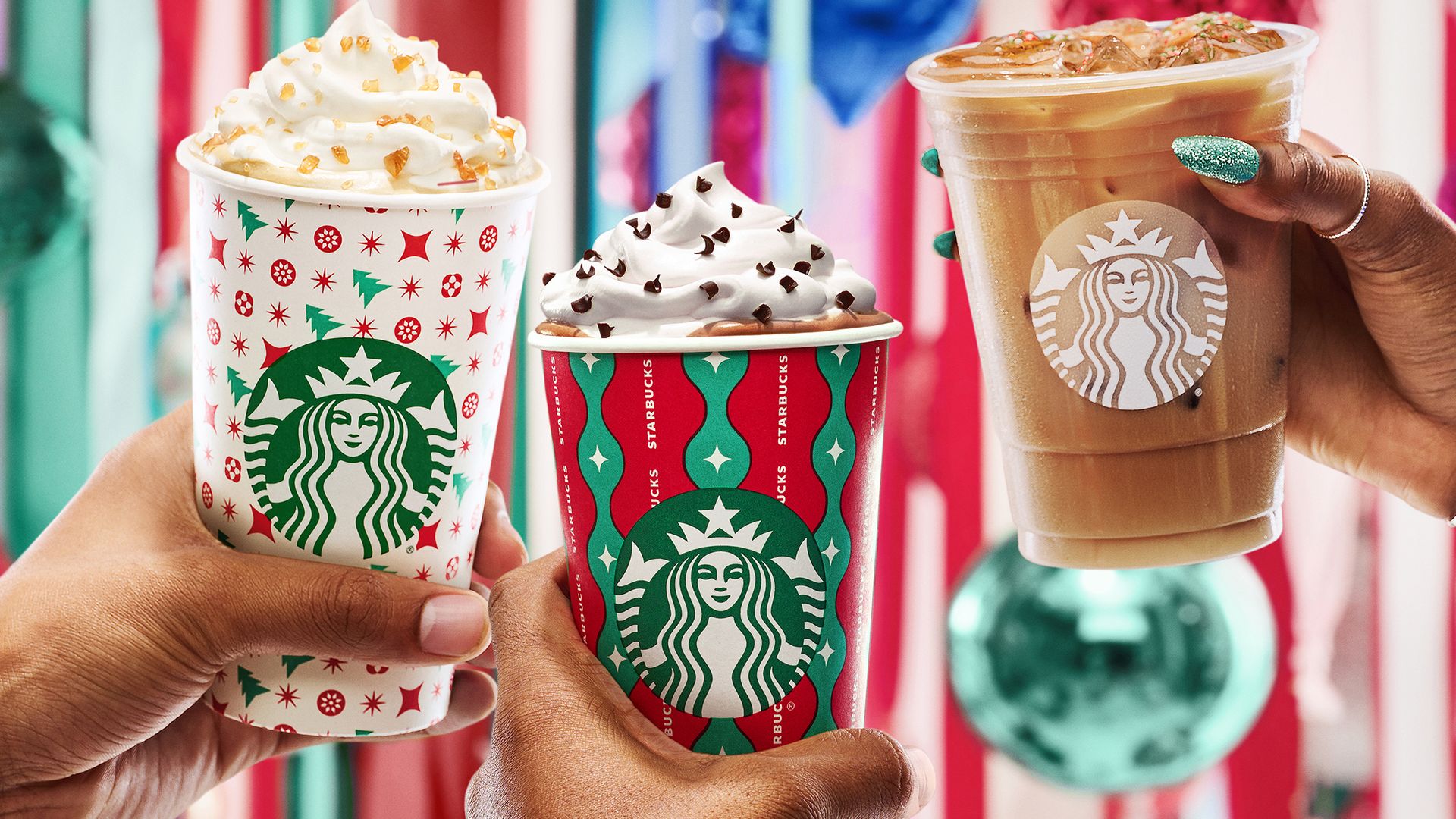 Hands holding Starbucks holiday drinks in decorative cups 