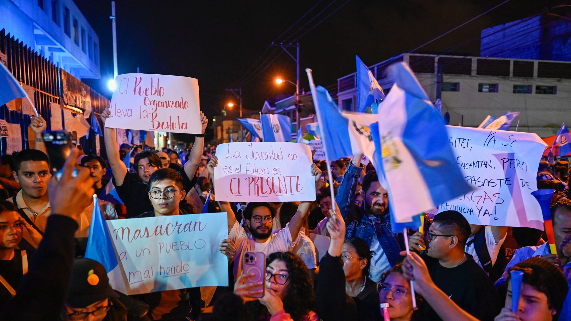 many protesters hold up signs and Guatemalan flags outside the attorney general's office in protest of a move against a party in the presidential election