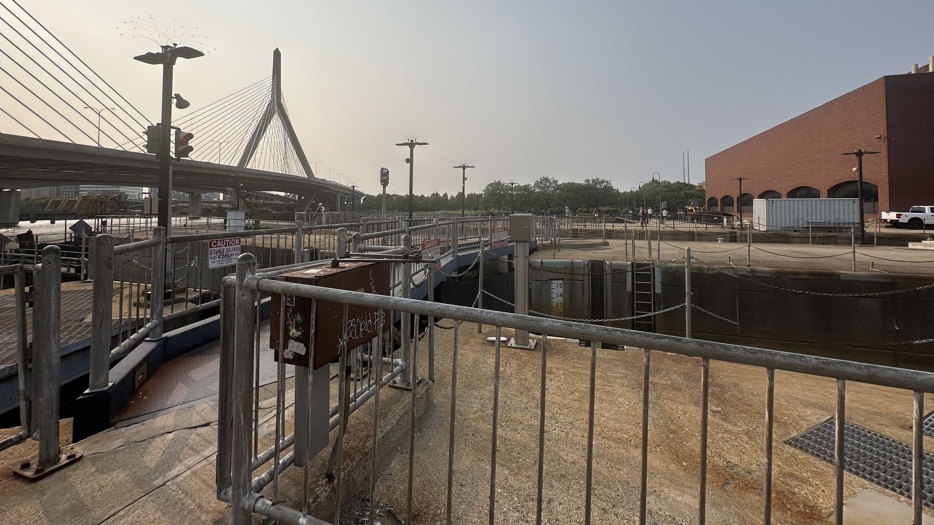 Empty canal lock with metal railings and a warning signs near a cable-stayed bridge in downtown Boston, known locally as the Charles River locks.
