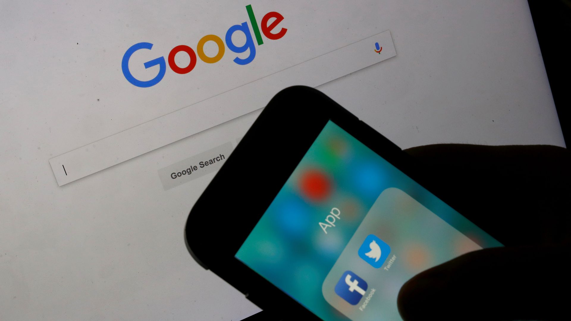 Google logo displayed on laptop behind Facebook and Twitter logos displayed on smartphone