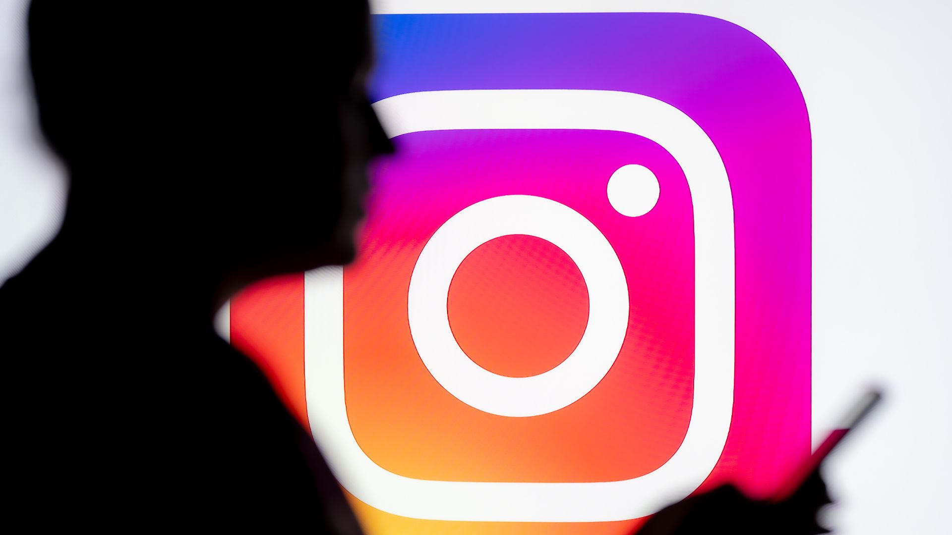 A person walks in front of the Instagram logo holding a cell phone.