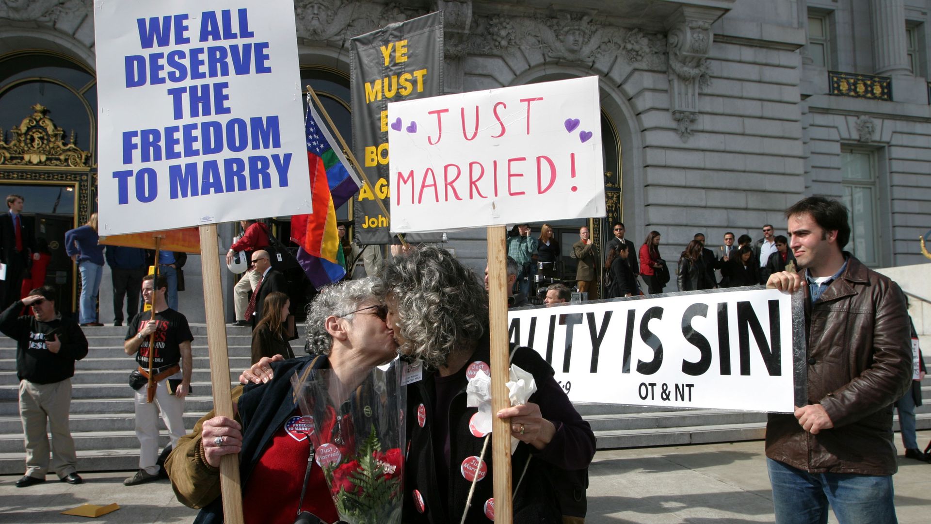 Photo of two women kissing as they hold signs that say "Just Married" and "We all deserve the freedom to marry" in front of City Hall