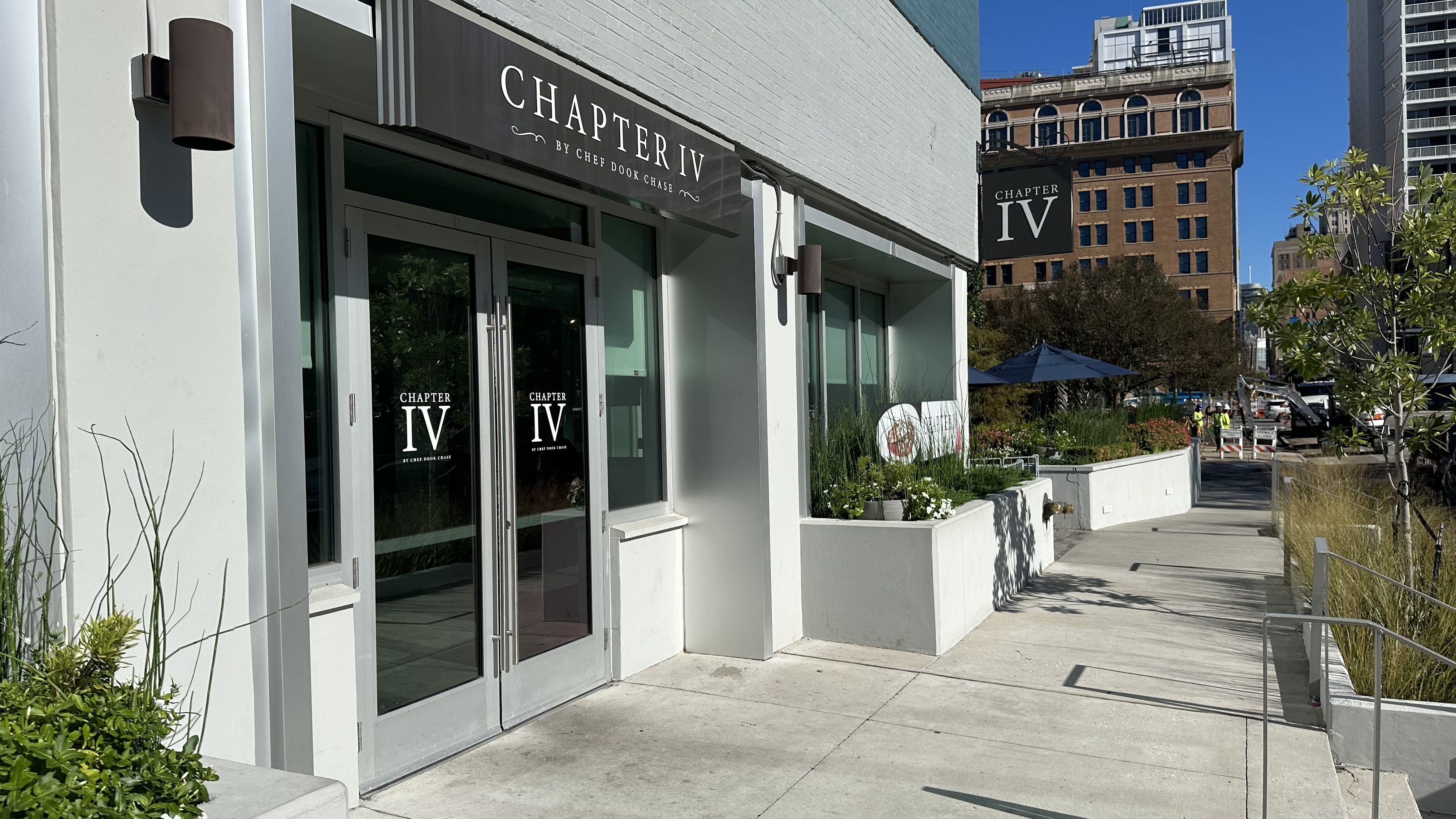 The corner of a building with large windows is seen during the middle of the day. Signage reads Chapter IV.